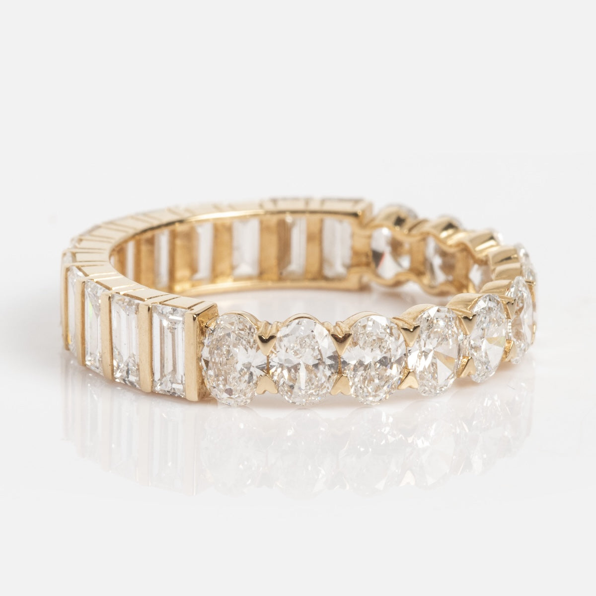 The Solid Gold Mixed Eternity Diamond Band Sample Size 7 is a 14k yellow gold ring with alternating oval and baguette-cut lab diamonds, shown on a white reflective surface.