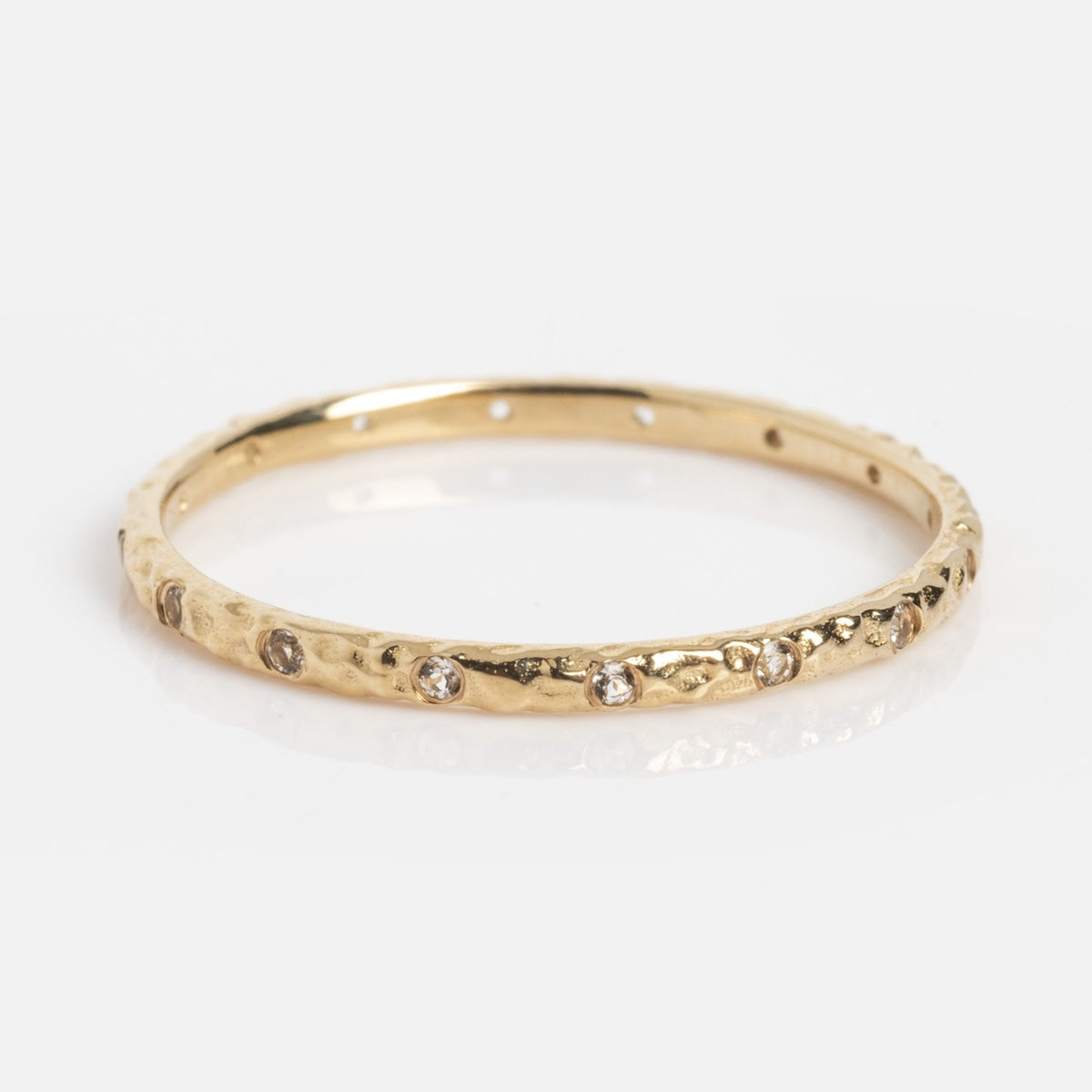 The Delicate White Topaz Stacking Ring (Sample Size 7) is a slim 1mm 9k solid yellow gold band with a hammered finish, adorned with evenly spaced small white topaz stones, shown against a white background.