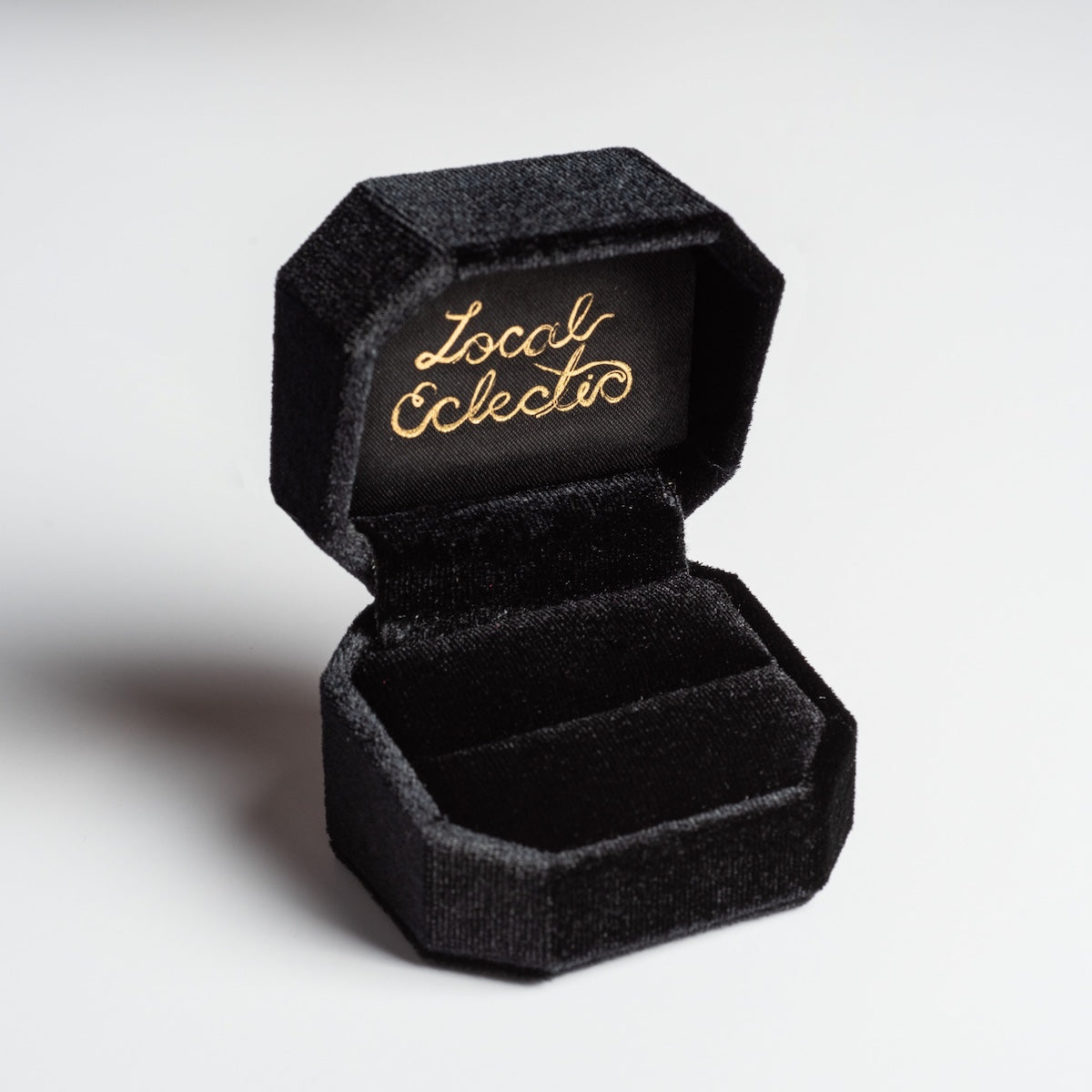 The Fancy Velvet Ring Box features an open octagonal design, gold cursive “Local Eclectic” inside the lid, and a plush black velvet interior.