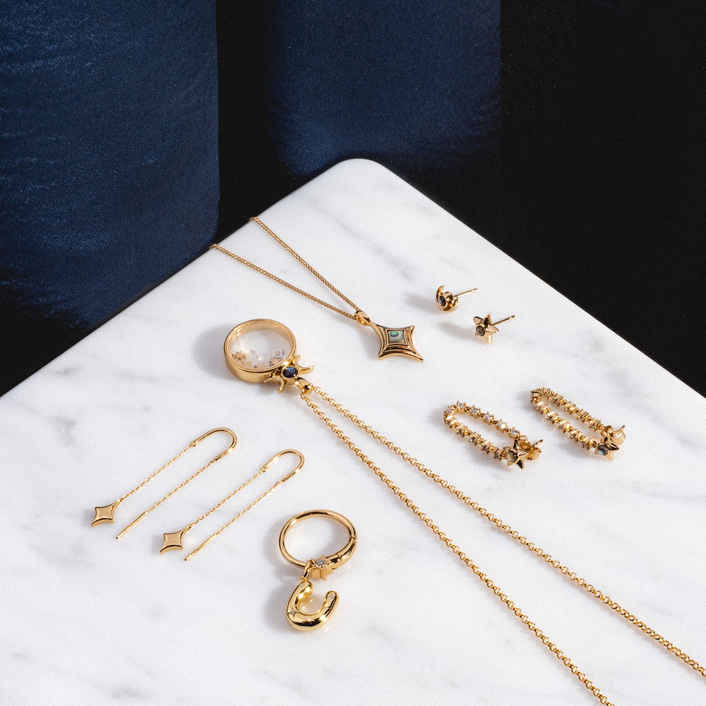 The Lucky Star Tennis Chain Earrings are displayed neatly on a white marble surface with a dark blue velvet background.