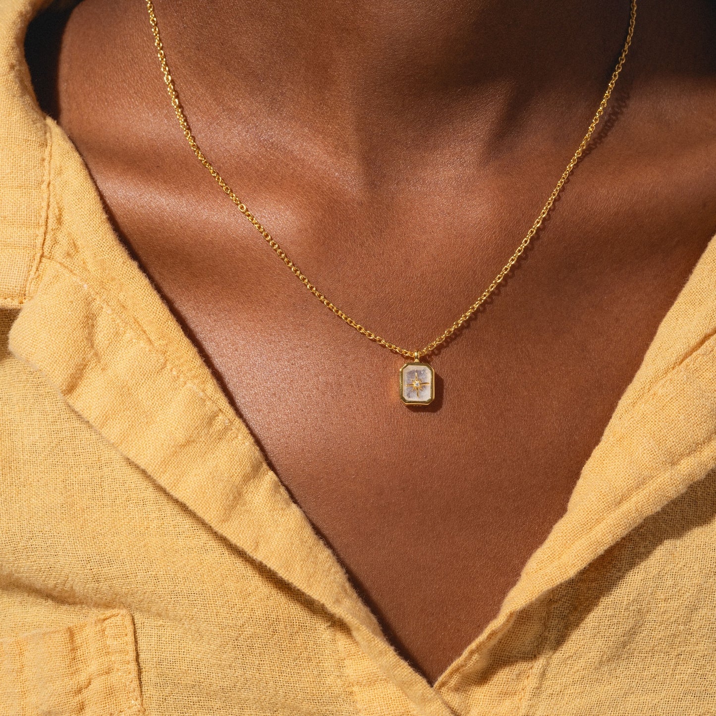 A close-up of a person wearing the Rainbow Moonstone & Diamond Manifest Your Dreams Pendant Necklace paired with a yellow collared shirt.