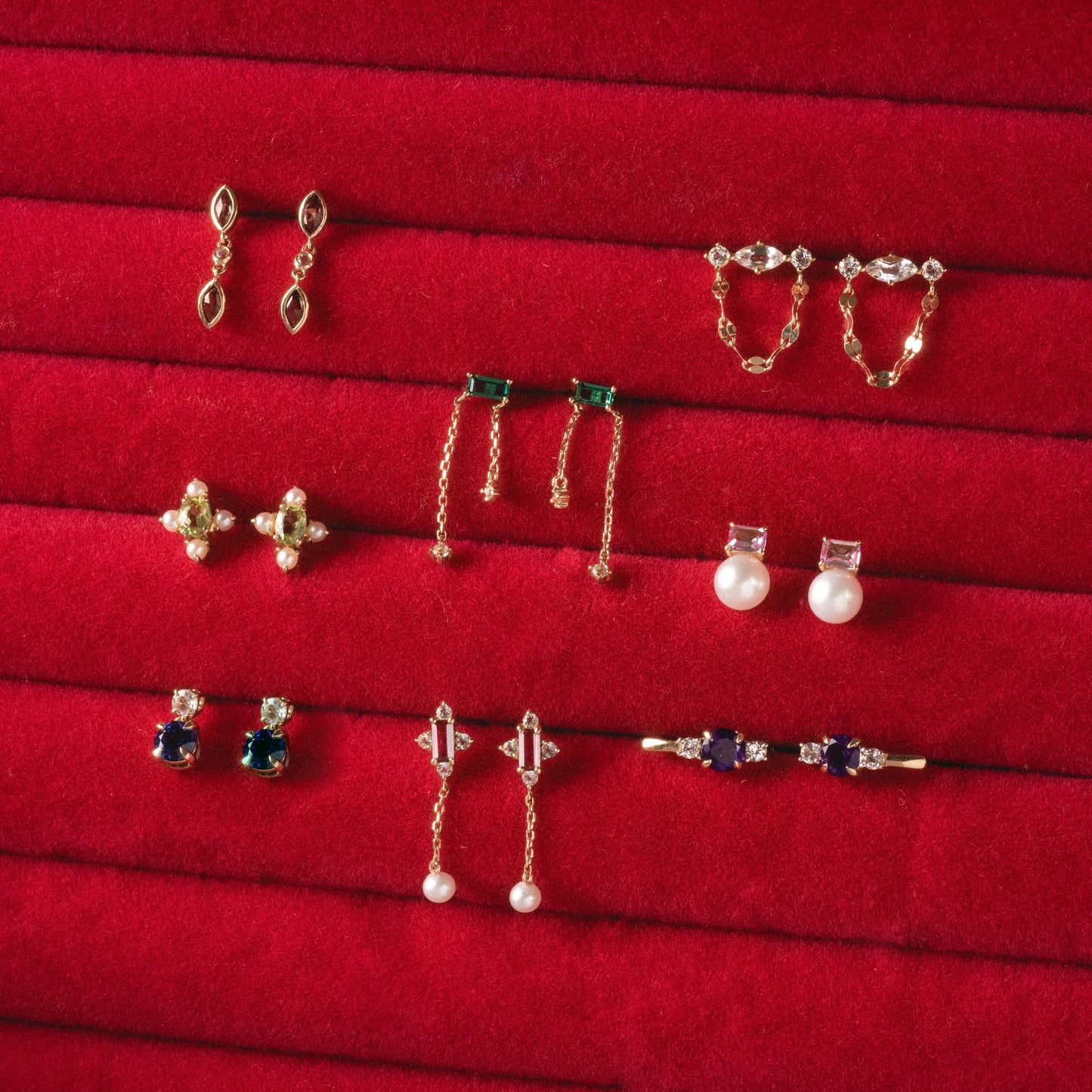 Nine pairs from the Solid Gold 2025 February Capsule Garnet Full Set, featuring gold, pearl, gemstone, and diamond styles with unique details, are beautifully arranged on a red velvet display. Free gift included.