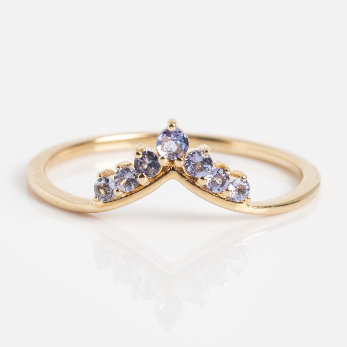 The Solid Gold 2025 December Capsule Delicate Arch Tanzanite Stacking Ring features a chevron-shaped gold band adorned with six small round blue tanzanites clustered in a graceful curve at the center.