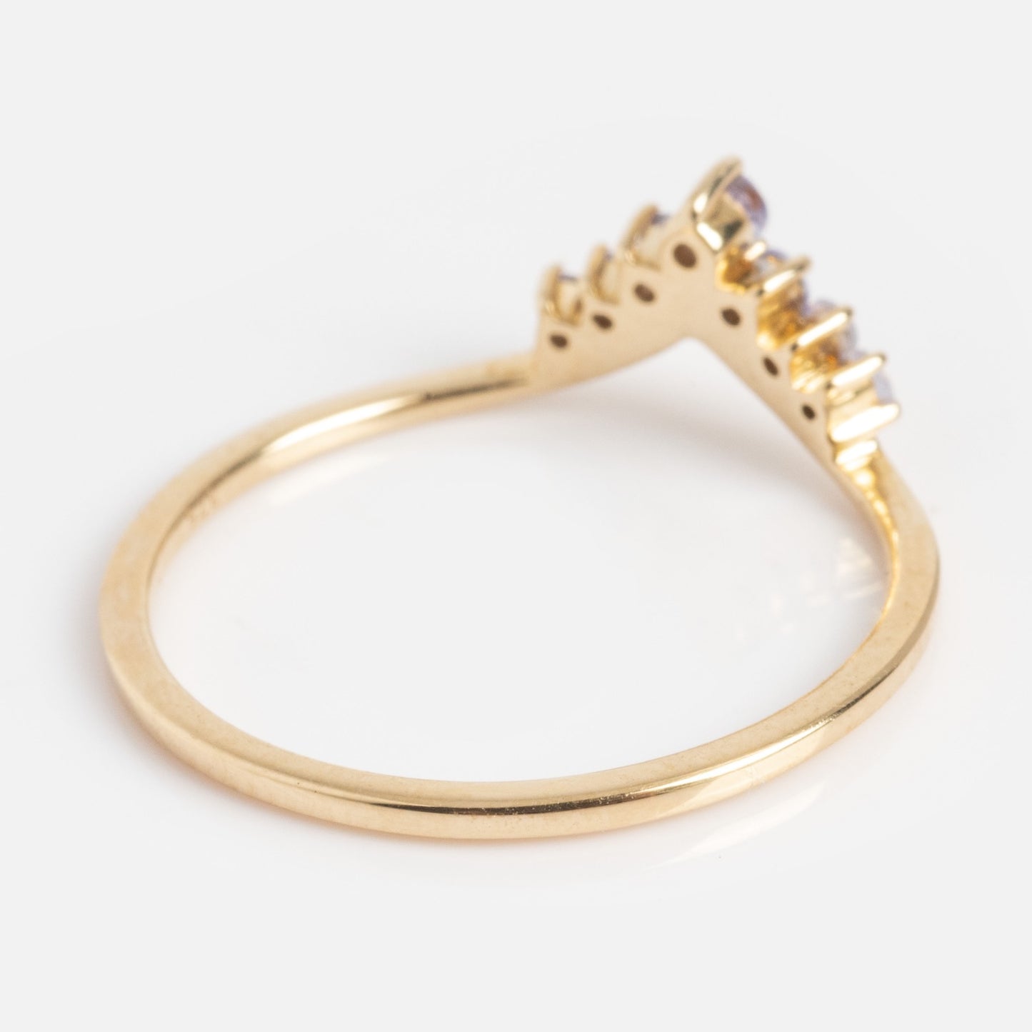 The Solid Gold 2025 December Capsule Delicate Arch Tanzanite Stacking Ring features a V-shaped gold band with tanzanite gemstones, shown on a white background.