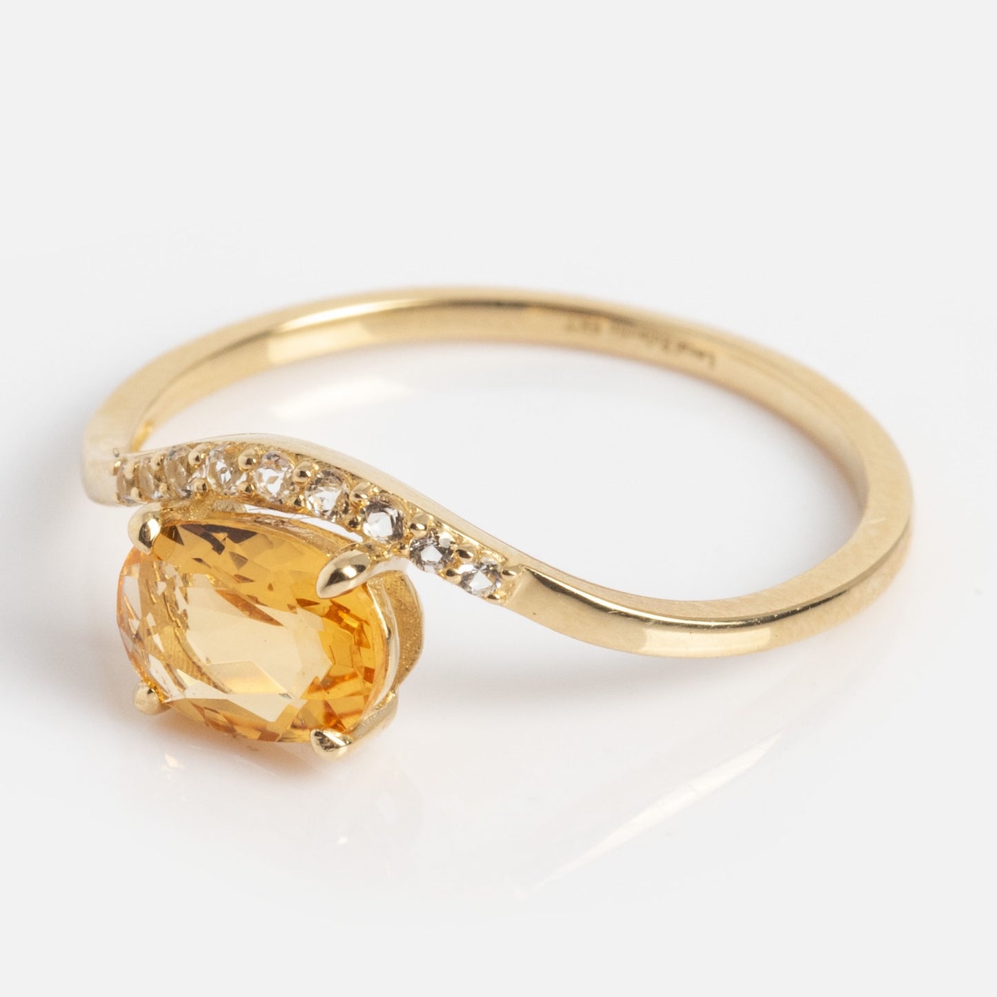 The Solid Gold 2025 November Capsule Floating Citrine Statement Ring features an oval yellow citrine center on a gold band, accented with small clear stones on one side, shown against a white background.