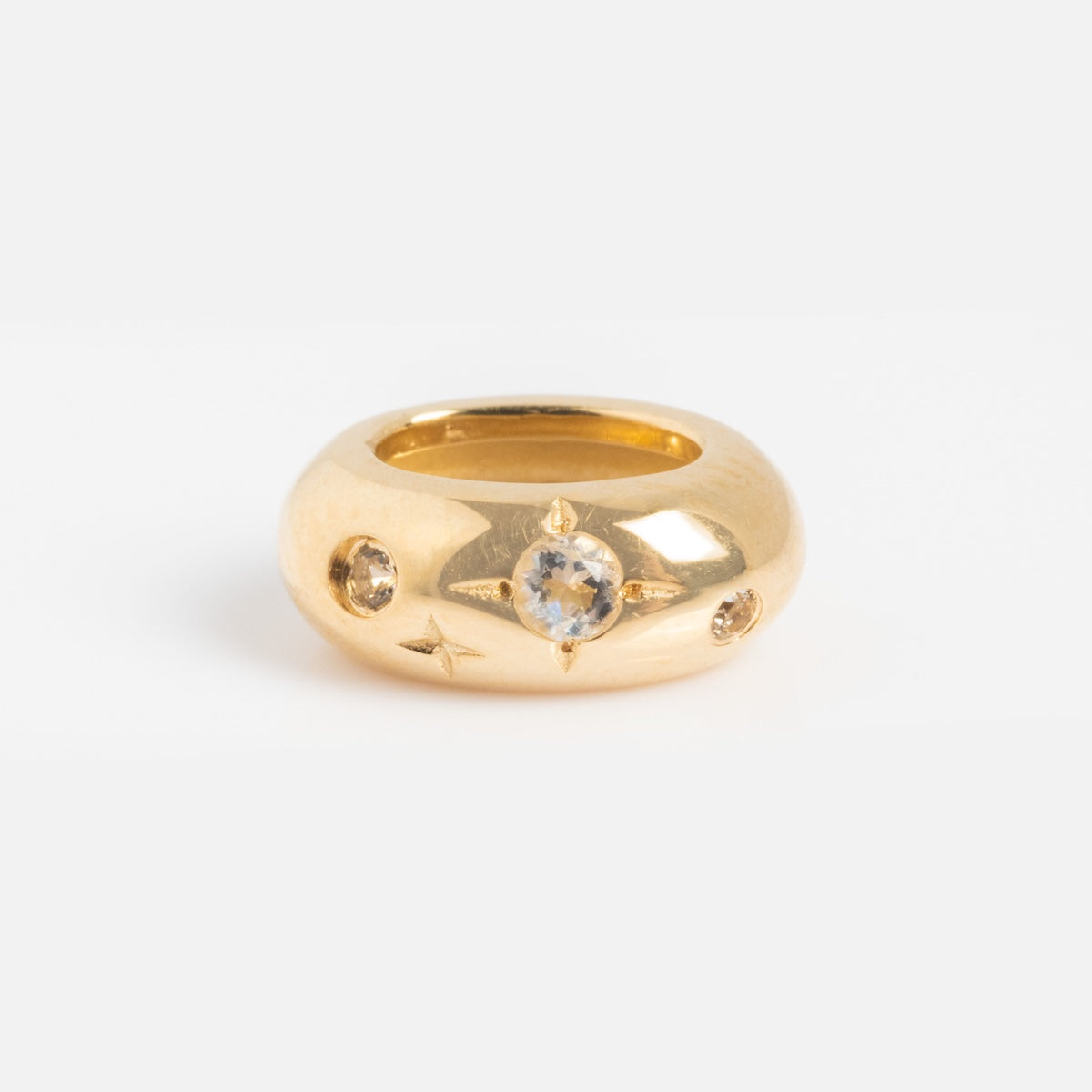 A chunky gold ring showcases a round, clear gemstone in a star-shaped setting, accented on each side by two Solid Gold Spacer Charms. Its smooth, polished finish adds an elegant touch.