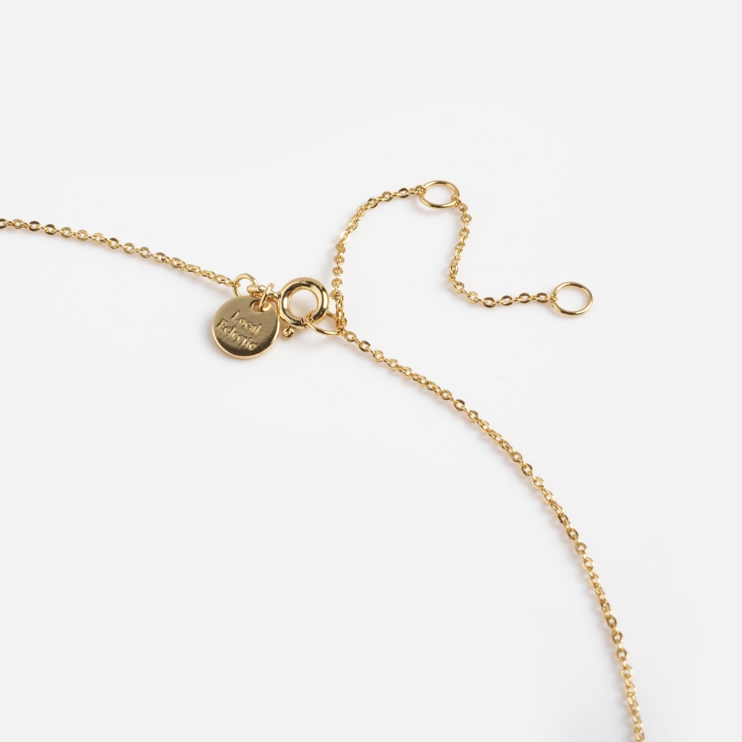 Close-up of the Buffy Dagger Necklace—a delicate gold chain with small round links, an adjustable clasp, and a round charm engraved with "merci maman," displayed on a plain white background.