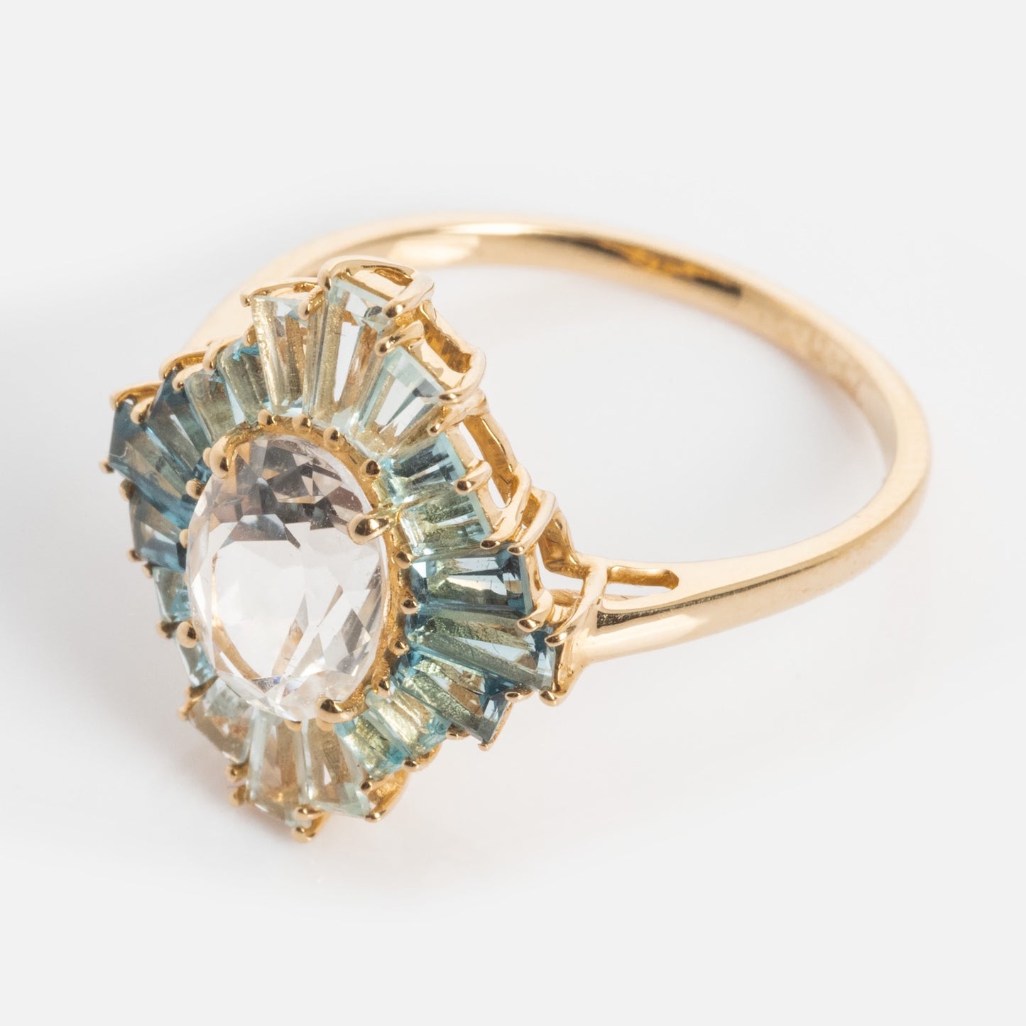 The 14k Bejeweled Blue Statement Ring features a large oval clear gemstone center, accented by a sunburst halo of rectangular blue and light green stones—perfect for making a bold style statement.