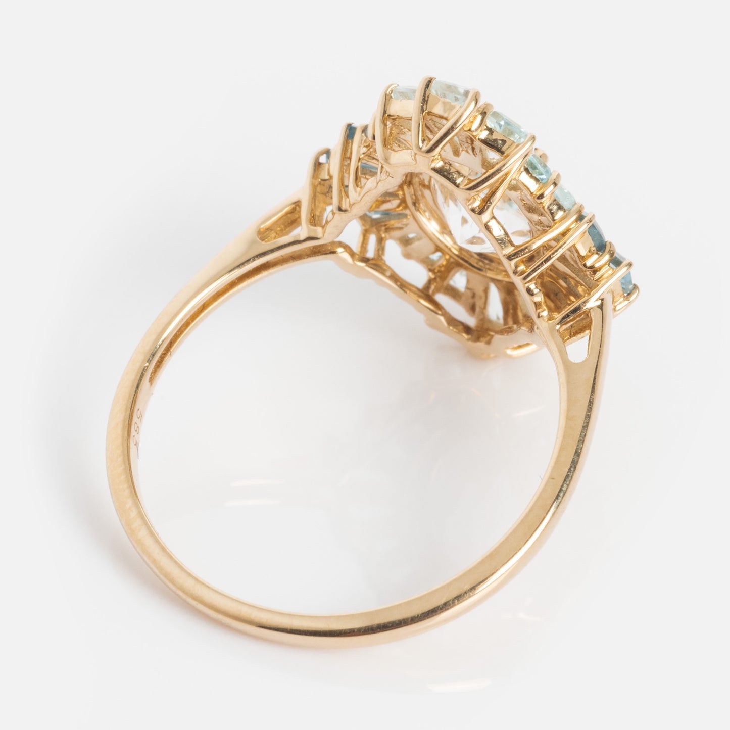 The 14k Bejeweled Blue Statement Ring features a thin 14k gold band and an intricate raised setting with multiple light blue gemstones, displayed from a side angle against a white background.
