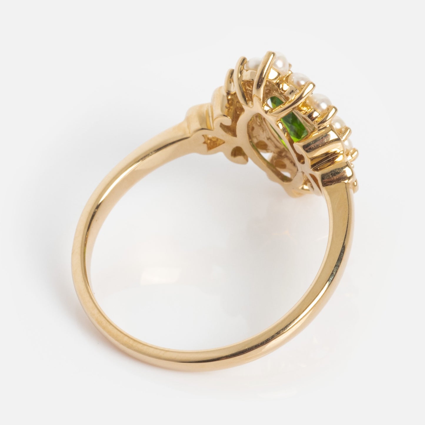 The 14k Opulent Green Diopside and Pearl Marquise Ring features an intricate gold setting with a marquise green diopside gemstone surrounded by a halo of small white pearls, shown from the side against a plain white background.