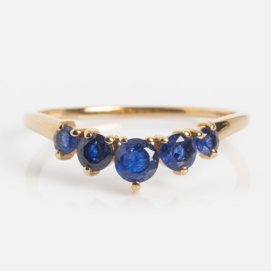 The 14k Blue Sapphire Arc Nesting Ring features five round blue sapphires of graduated sizes set in a row on a simple, polished yellow gold band.