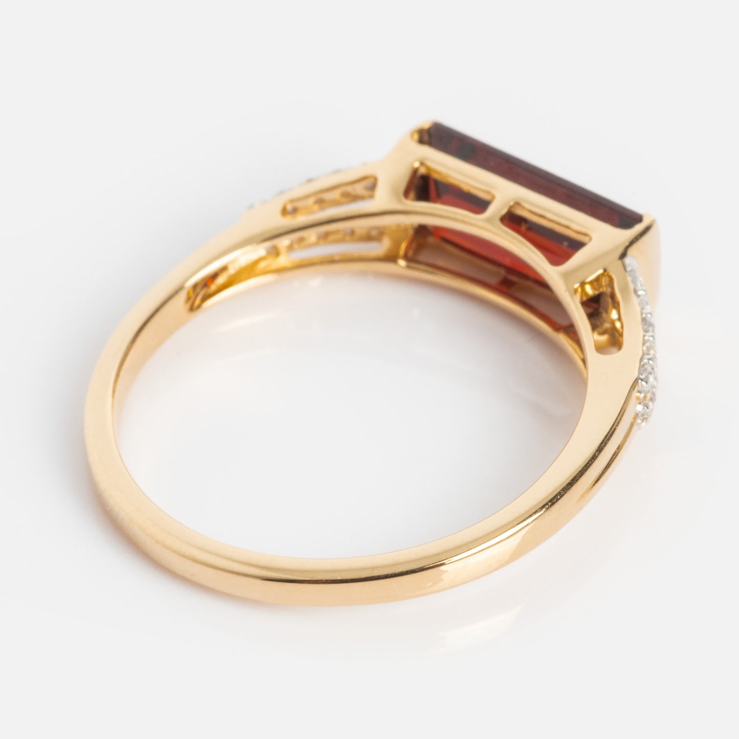 The 14k Gilded Garnet East West Baguette Ring features a large rectangular red gemstone set horizontally, accented by small clear stones along one side of the band, displayed against a white background.