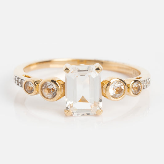 The 14k Vintage Inspired Majesty Ring showcases a large emerald-cut clear center gemstone, three round diamonds on each side, and extra diamonds set along a polished gold band for added brilliance.