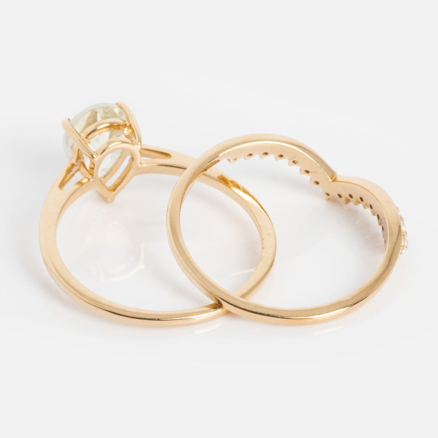 The 14k Classic Green Grandeur Nesting Ring Set features a green sapphire solitaire ring and a matching curved band, both crafted in 14k gold and designed to fit perfectly together on a white surface.