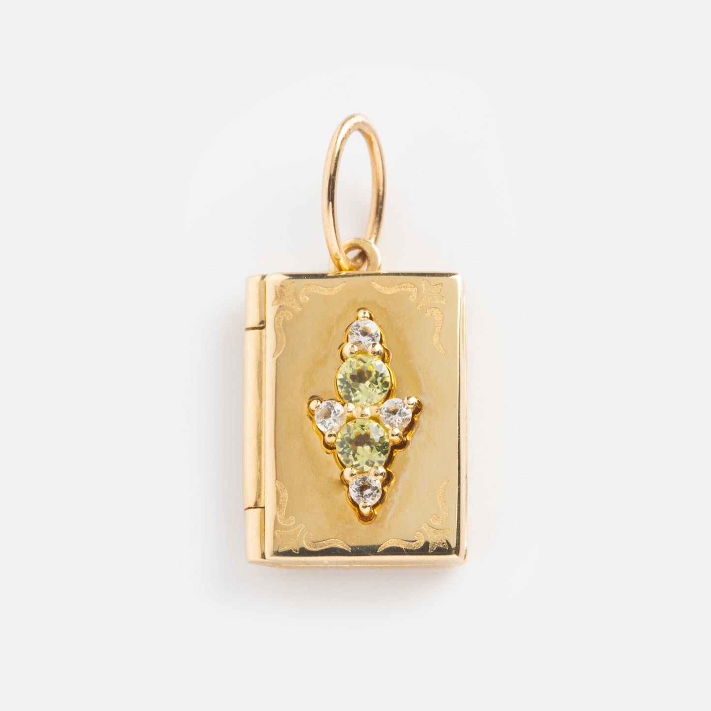 The Solid Gold Amulet Charm is a Local Eclectic exclusive: a gold book-shaped locket with engraved edges, a cross design, and green and clear gemstones—perfect to add to your favorite gemstone necklace.