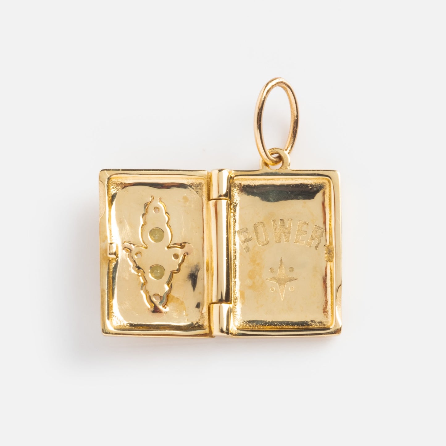 The Solid Gold Amulet Charm is a local eclectic exclusive: a book-shaped gold locket, open to reveal three green stones on one side and POWER engraved on the other—an intricate, collectible design.