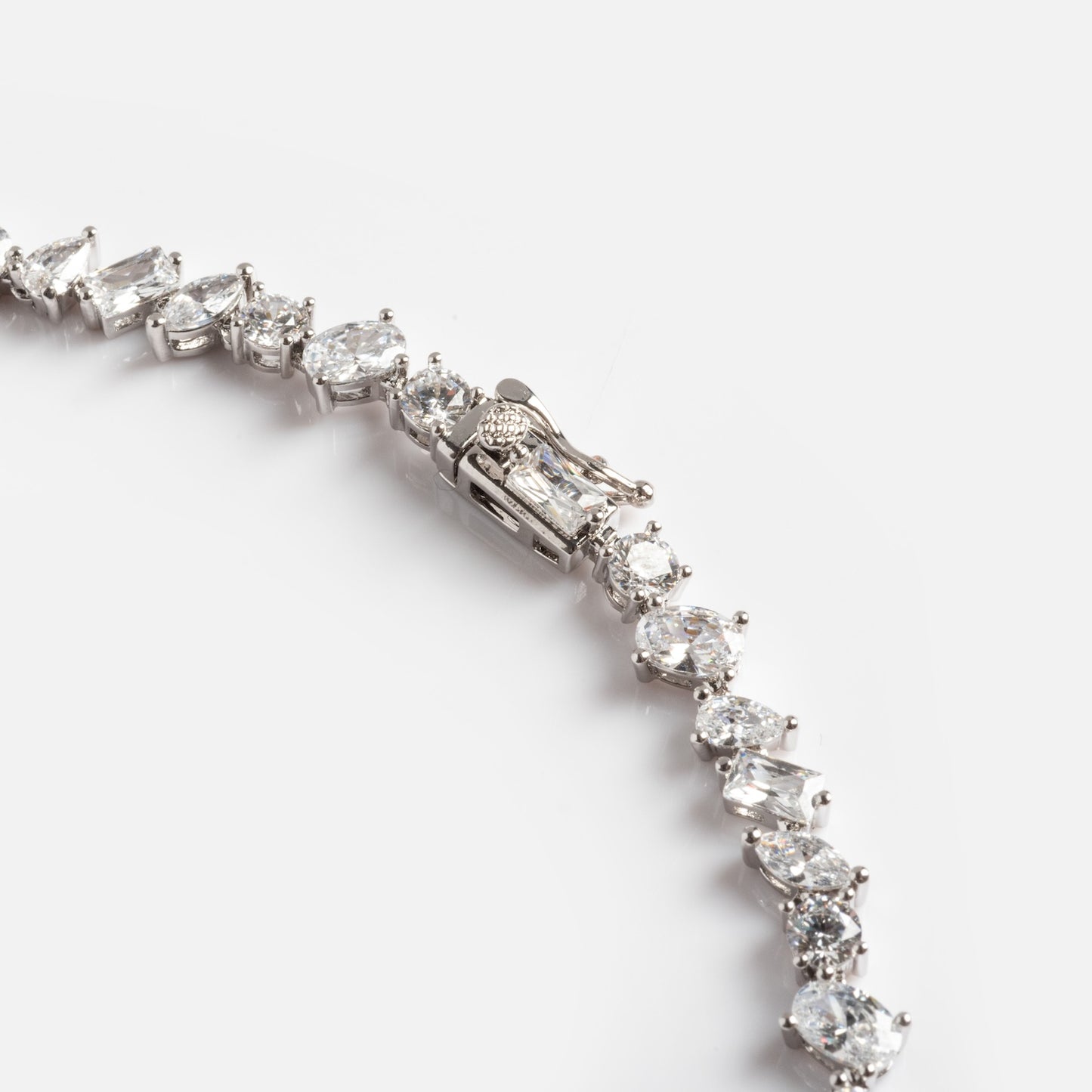 A close-up of the Pear Diamond Tennis Necklace featuring oval and emerald-cut clear gemstones, displayed on a white background with the clasp visible.