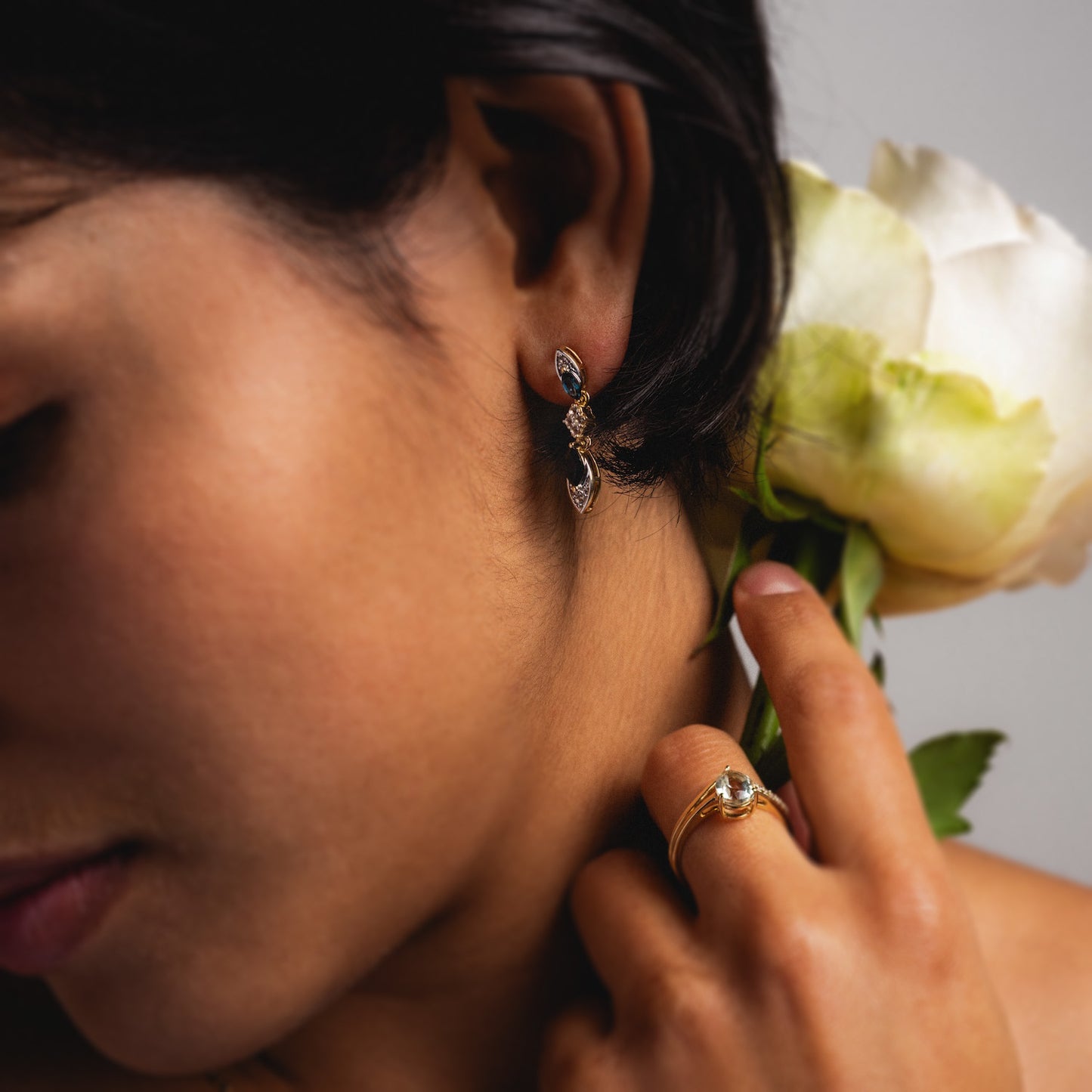 A close-up of a person wearing 14k Vintage Inspired Statement Drop Earrings, holding a white rose near their ear. The image highlights the earrings and the flower.