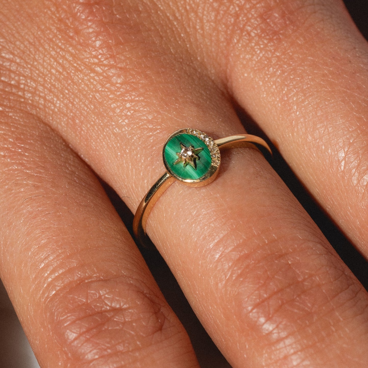 A close-up of a hand wearing the Solid Gold Crystal Crescent Moon Ring for Manifestation, featuring a green oval stone centerpiece, delicate star-shaped detail, and tiny gemstone—an ideal ring for manifestation.