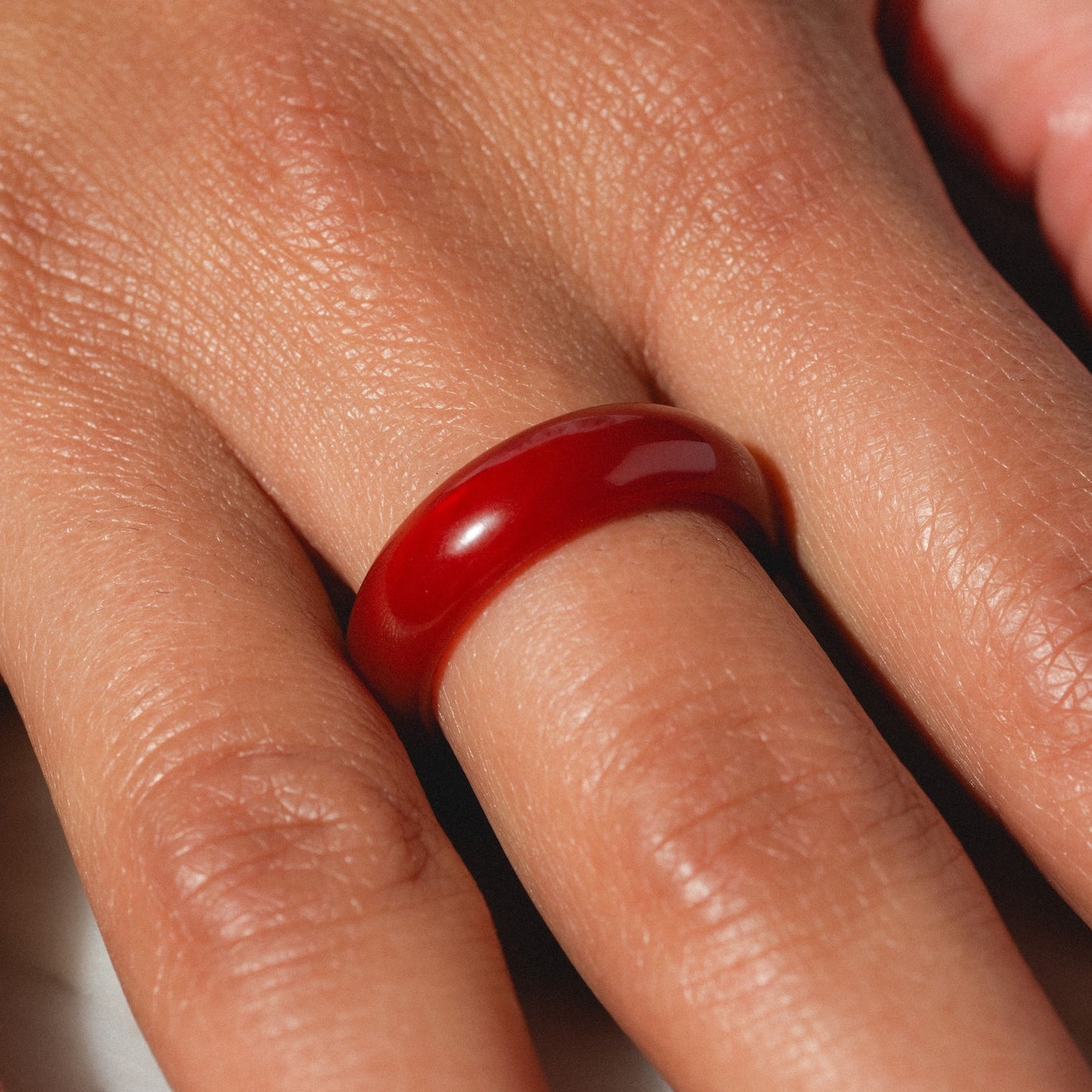 A close-up of a hand wearing the Persimmon Dark Orange Agate Stone Ring (size 8), a smooth, shiny 5.8 mm band featuring natural agate with visible skin texture and lines for an elegant, authentic look.