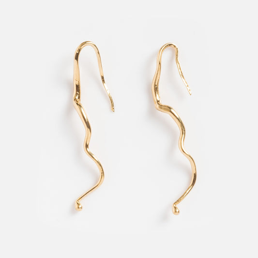 The Line Study Earrings are gold-plated, wavy, snake-like drop earrings with a shiny finish, shown against a plain white background.