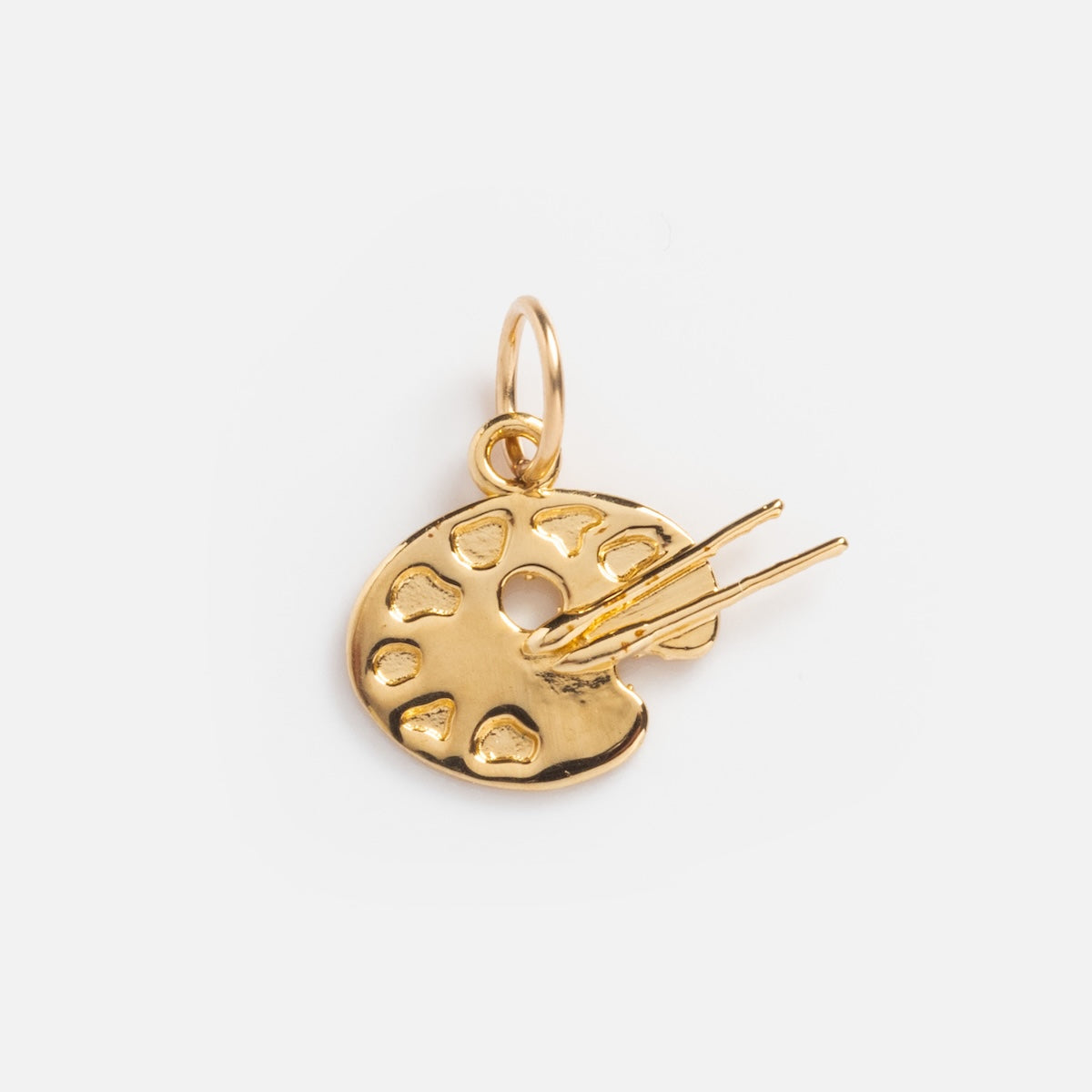 The Charms by I Like It Here Club features a gold artist’s paint palette and two paintbrushes, crafted with 12k yellow gold plating, displayed on a plain white background.