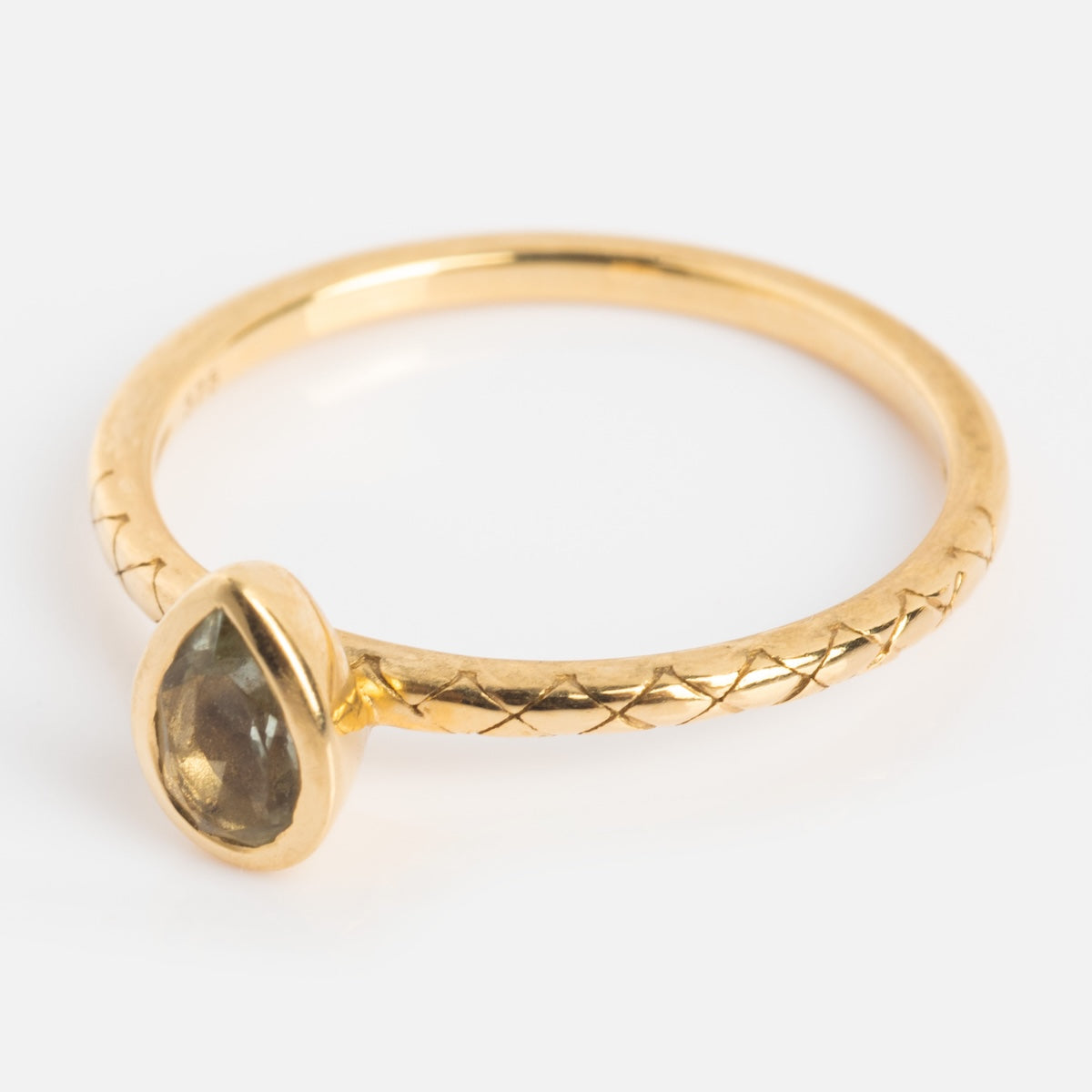 A solid gold ring with a thin band, engraved crisscross pattern, and a bezel-set pear-shaped green amethyst stone.