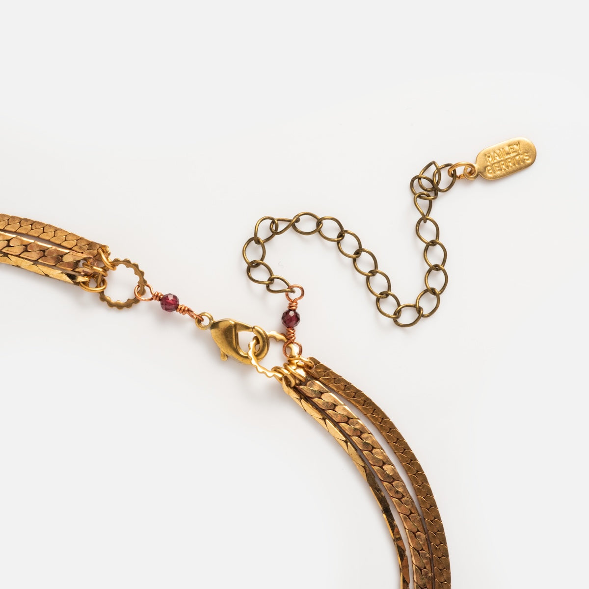The Palmer Gemstone Necklace features recycled brass chains layered with small red garnet beads, an adjustable extension, and a gold tag engraved with ABLE CRAFTS. Stylishly displayed against a white background.