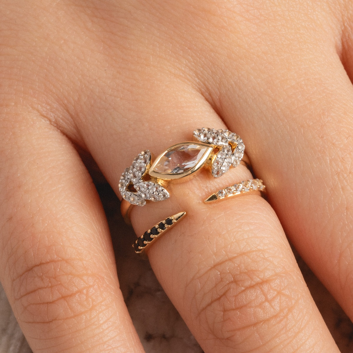 A hand wears two gold rings: a 14k gold ring with a marquise-cut central stone and pavé white stones, plus the 14k Black and White Open Front Nesting Band.