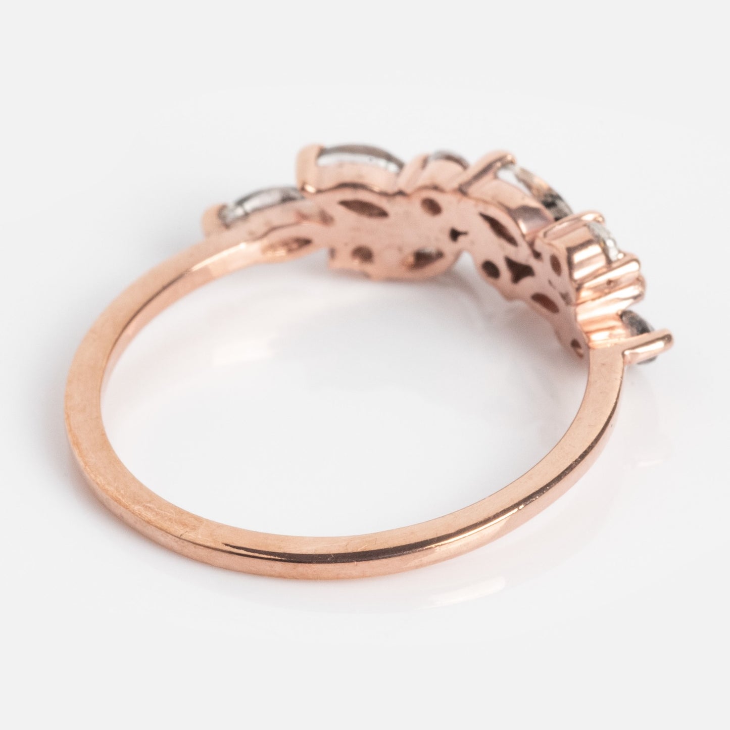 The Gemstone Orchard Ring features a thin rose gold band and ornate setting with multiple gemstones, including sparkling London blue topaz, shown from the side on a white background.