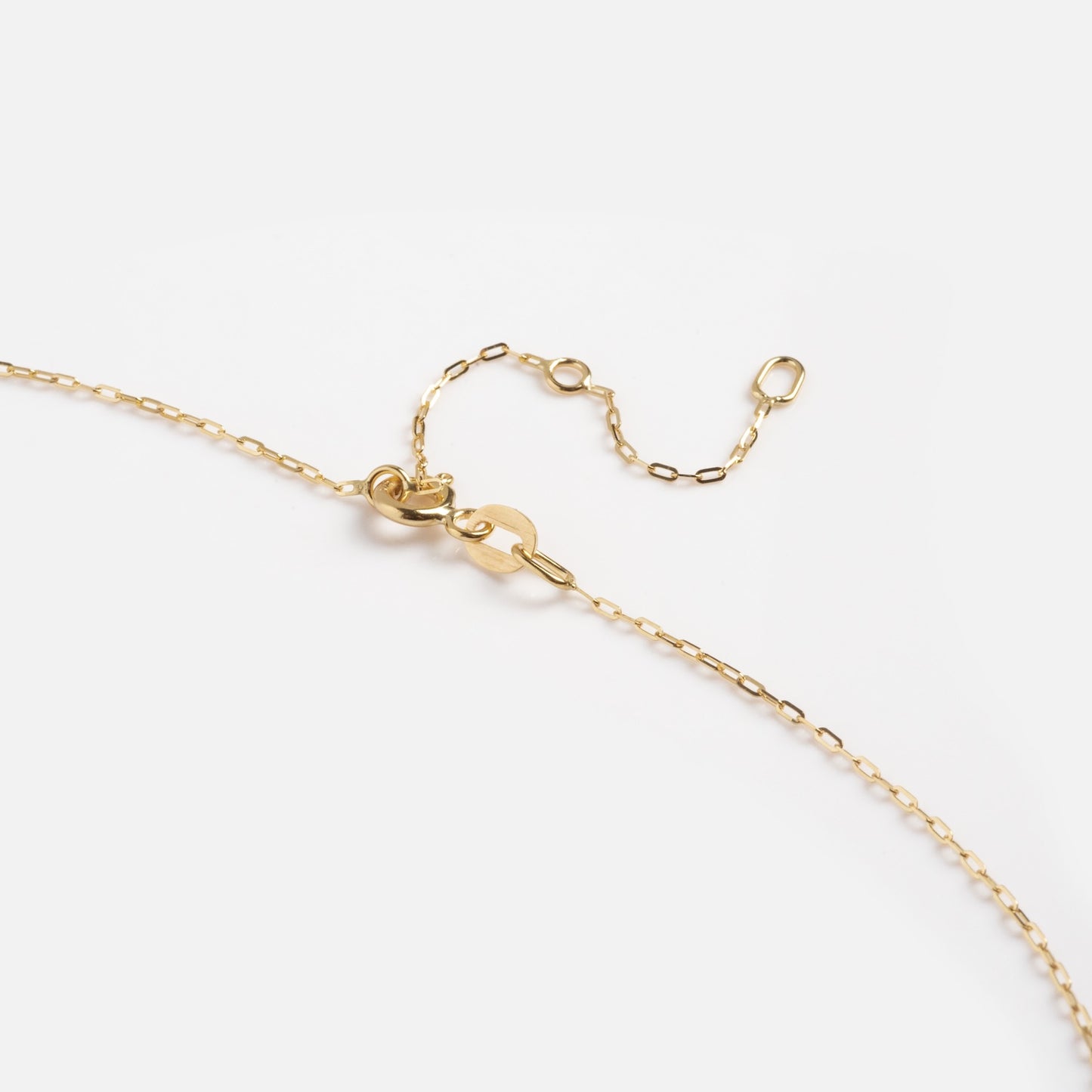A close-up of the Solid Gold Delicate Paperclip Chain, featuring a lobster clasp and short extension chain, displayed on a white background.