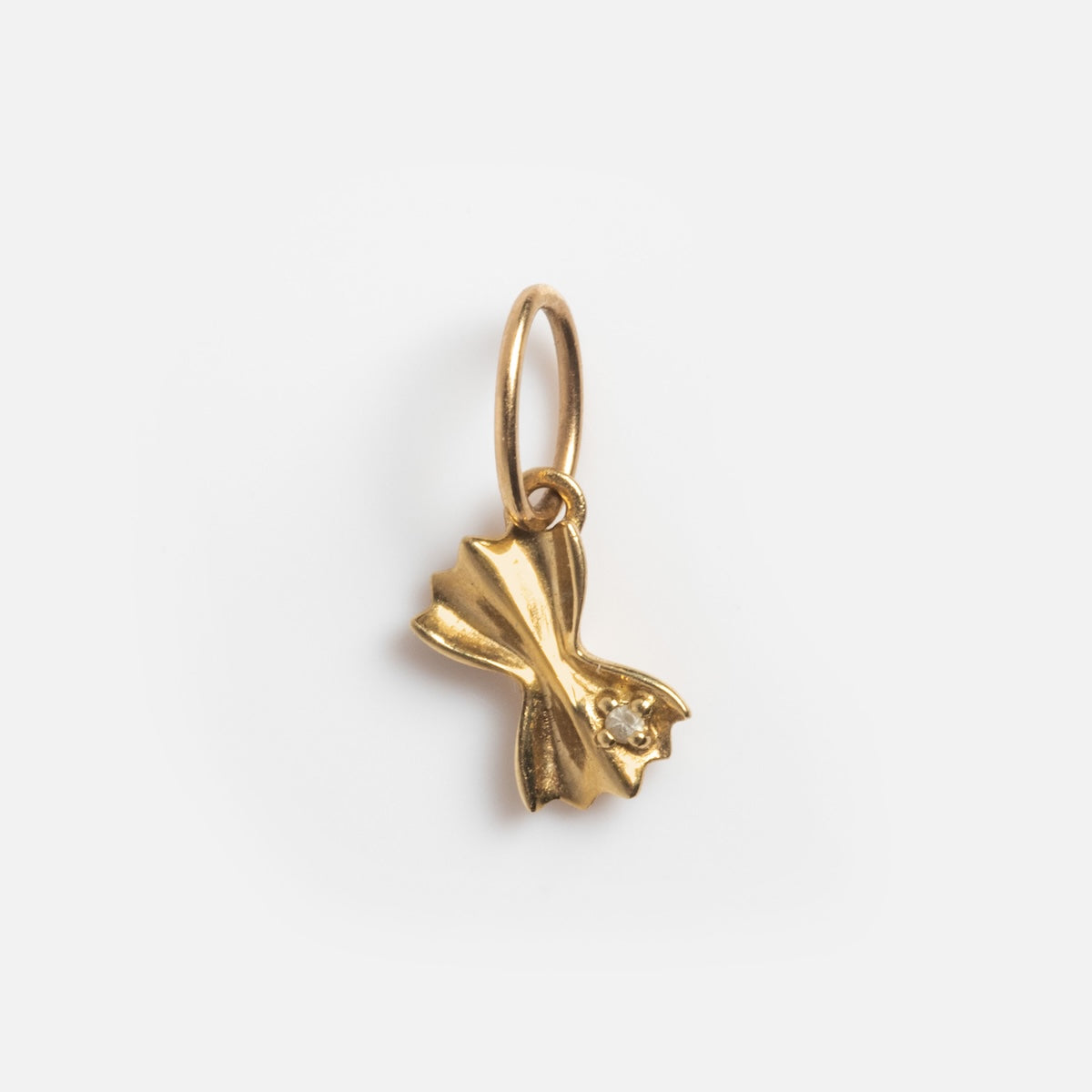 The Solid Gold Foodie Charm is a 9k yellow gold bowtie pasta-shaped charm with a small round gem in the center, attached to a simple gold loop—an eye-catching piece for any solid gold charms collection.