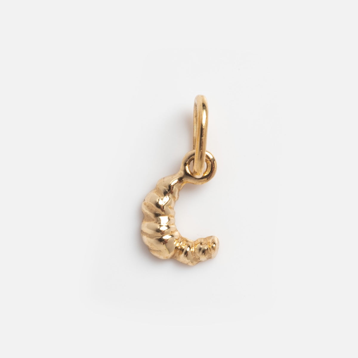 The Solid Gold Foodie Charm is a small croissant-shaped pendant crafted in 9k yellow gold, featuring a top loop for attaching to jewelry, displayed on a plain white background.