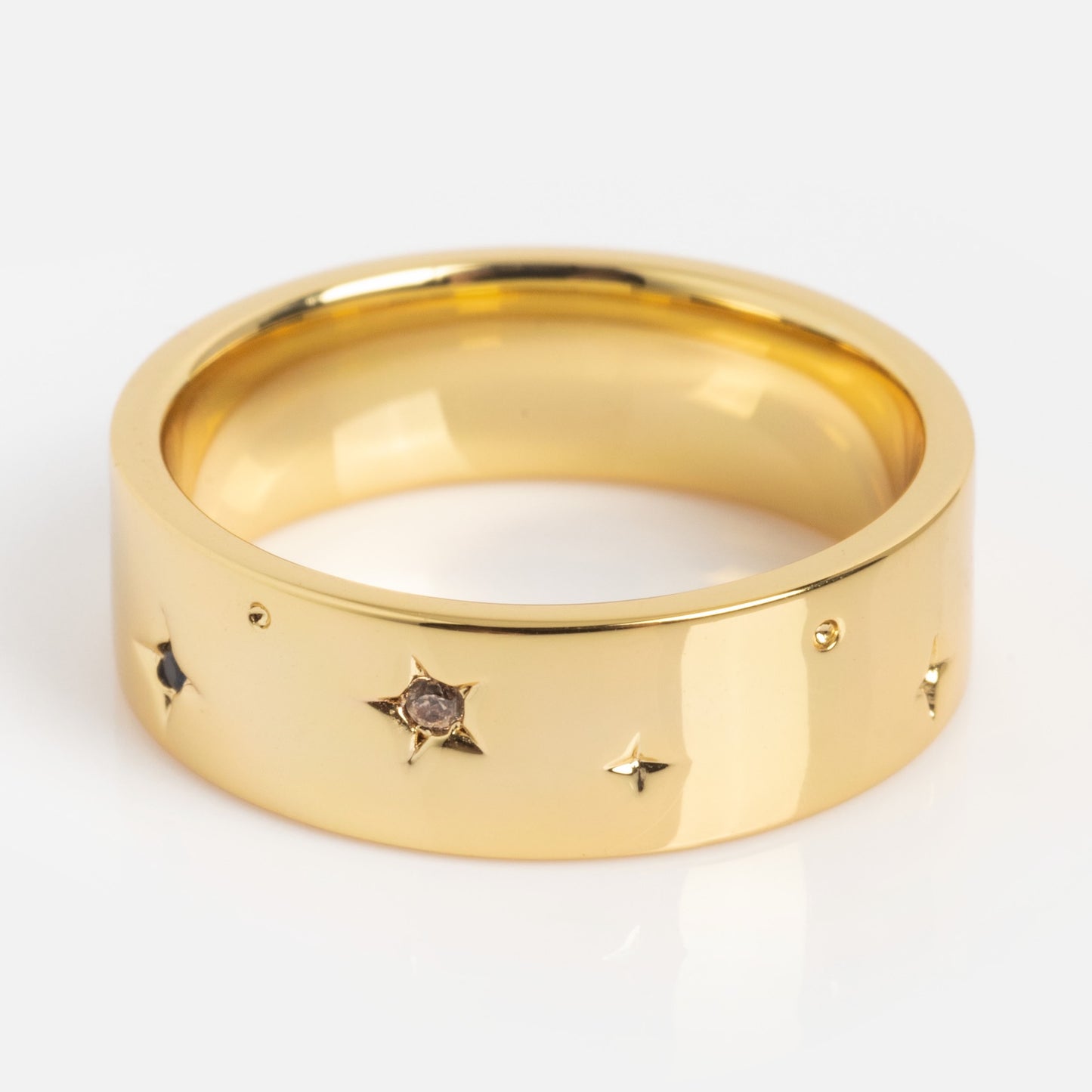 The What the Fuck Cigar Band is a wide gold ring with a smooth, polished finish, adorned with small star-shaped engravings—some set with tiny gemstones.