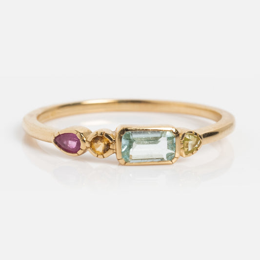 The Solid Gold First Light Pastel Gemstone Ring features a rectangular aquamarine centerpiece, with a round yellow stone, a light green stone, and a pear-shaped pink stone set in solid gold on a white background.