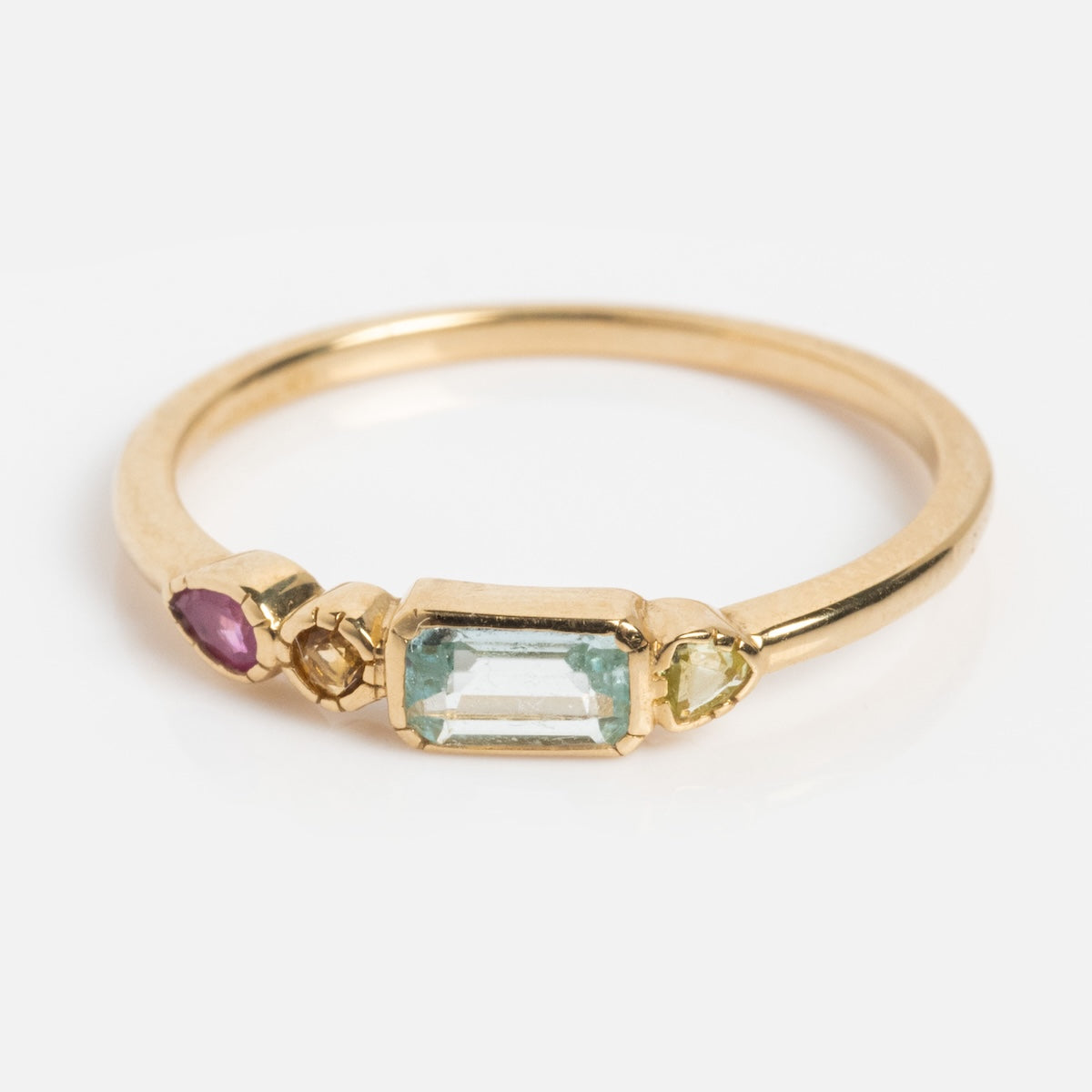 The Solid Gold First Light Pastel Gemstone Ring features a rectangular light blue gem, round yellow gem, small round champagne-colored gem, and an oval pink gem set in a minimalist solid gold band.