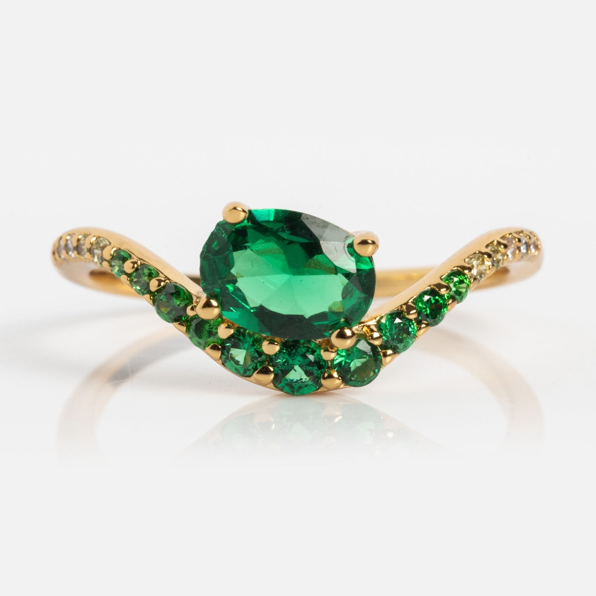 The Main Character Floating Ombre Birthstone Ring showcases an oval green gemstone center with smaller round green stones on a curved gold band, creating a radiant gradient effect.