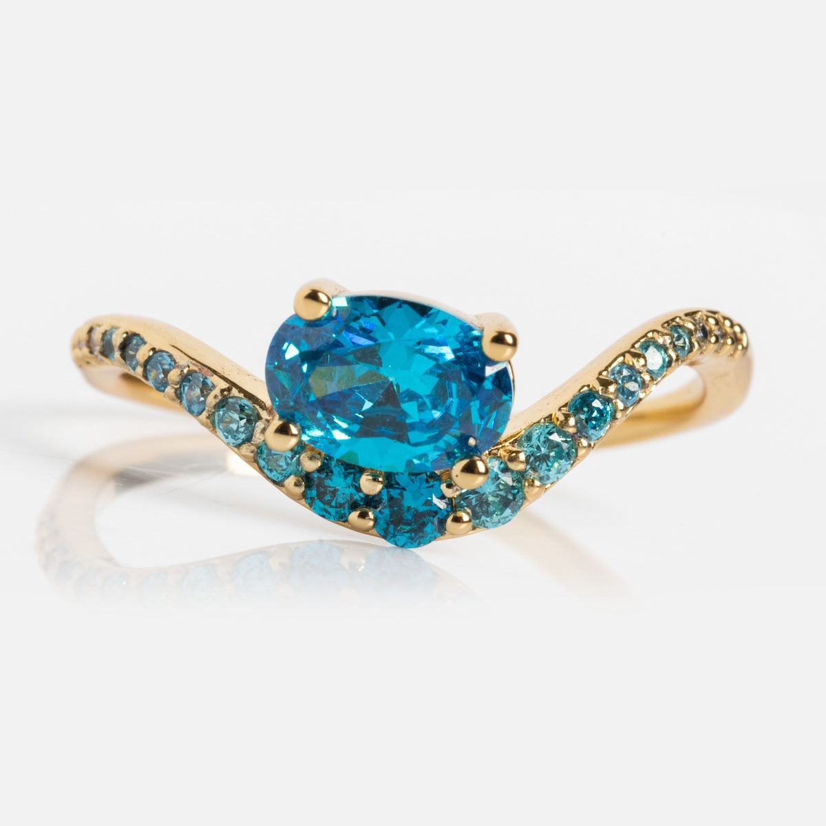 The Main Character Floating Ombre Birthstone Ring features a large oval blue center stone with smaller round blue gems on a wavy gold band, displayed on a white background—an elegant piece of birthstone jewelry.