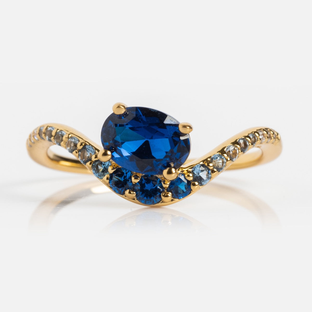The Main Character Floating Ombre Birthstone Ring features a large oval blue sapphire floating at the center, accented by blue and white gems in a wave design on a gold band—an elegant birthstone jewelry piece.