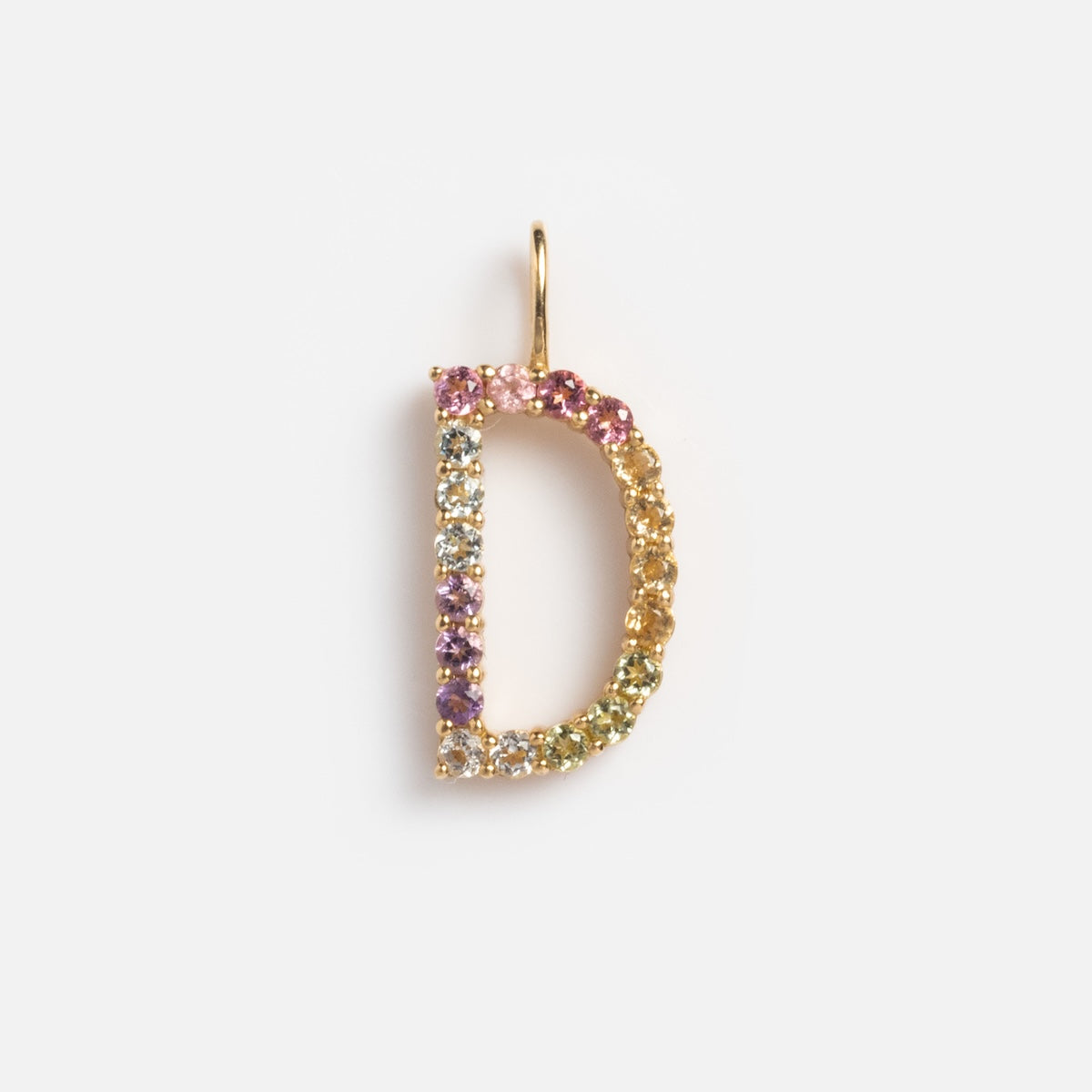 The Solid Gold Pastel Gemstone Letter Charm Sample is a 9k yellow gold pendant shaped like the letter D, adorned with multicolored gemstones including pink tourmaline, shown against a plain white background.