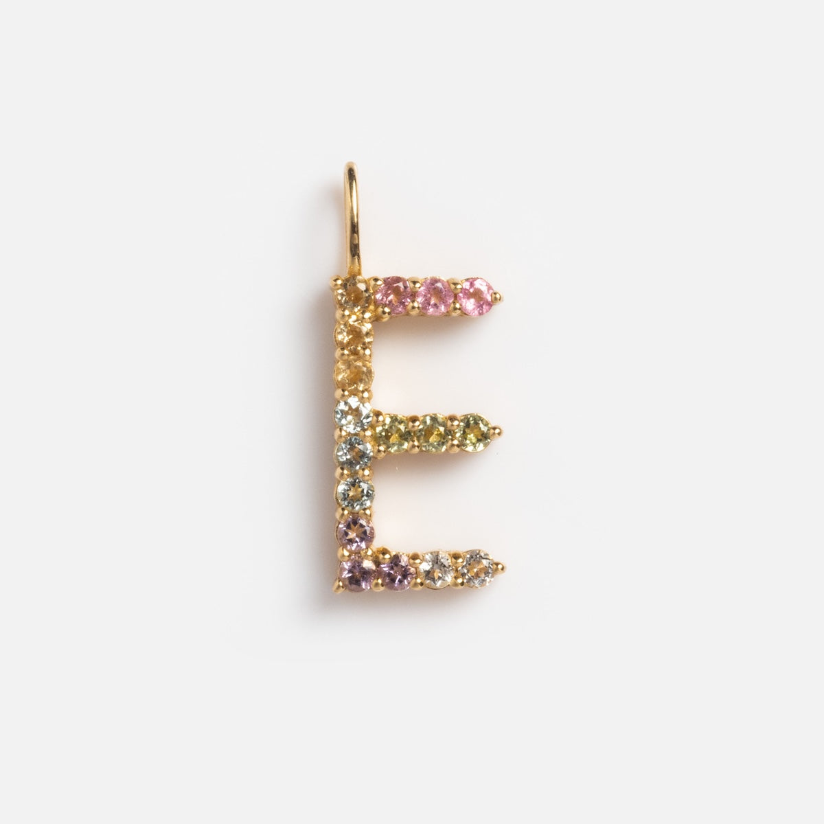 The Solid Gold Pastel Gemstone Letter Charm Sample is a 9k yellow gold pendant shaped as E, featuring multicolored gemstones—pink tourmaline, green, blue, and clear stones—shown on a plain white background.