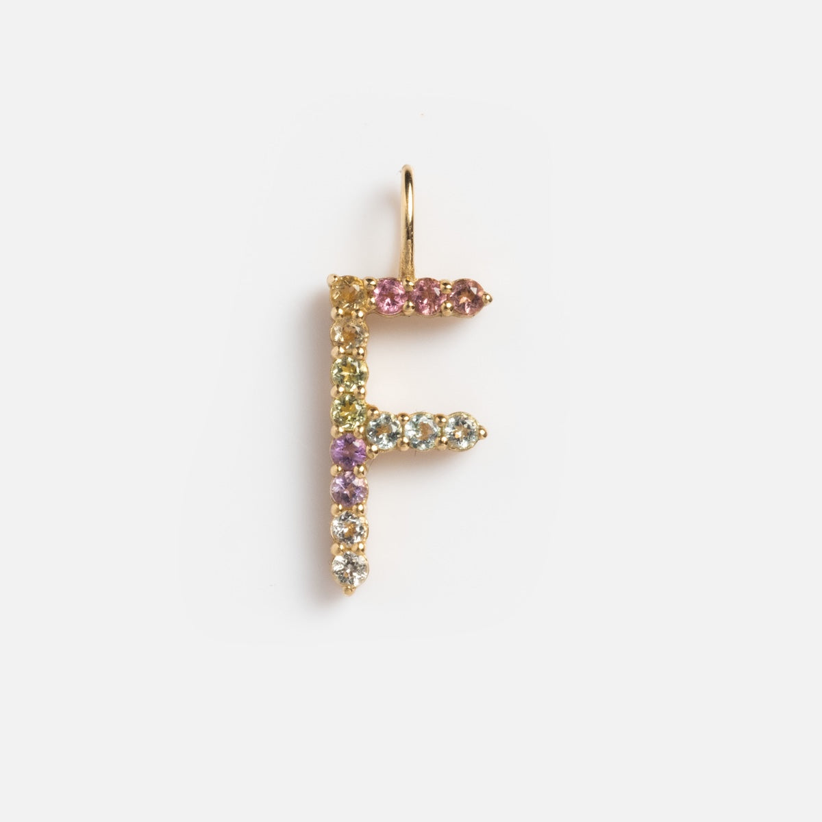 The Solid Gold Pastel Gemstone Letter Charm Sample is an F-shaped pendant in 9k yellow gold, adorned with pink tourmaline plus purple, green, and blue gemstones, displayed on a plain white background.