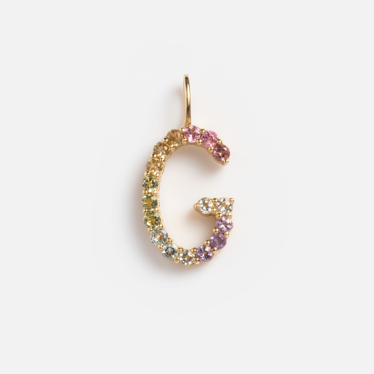 The Solid Gold Pastel Gemstone Letter Charm Sample is a 9k yellow gold pendant shaped like G, adorned with pastel multicolored gemstones such as pink tourmaline, shown on a simple white background.