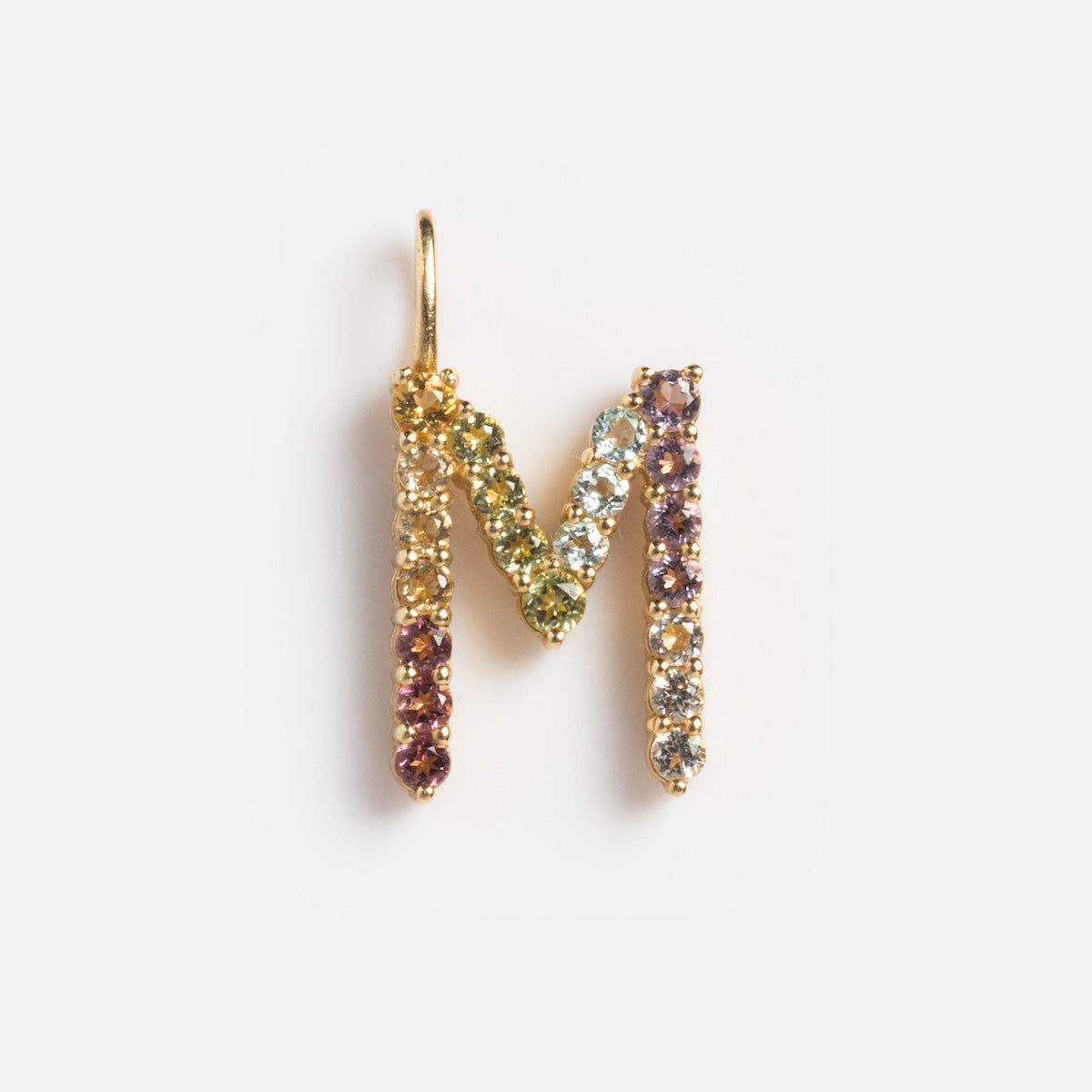 The Solid Gold Pastel Gemstone Letter Charm Sample, shaped like the letter M and adorned with multicolored gemstones including pink tourmaline, is displayed against a plain white background.