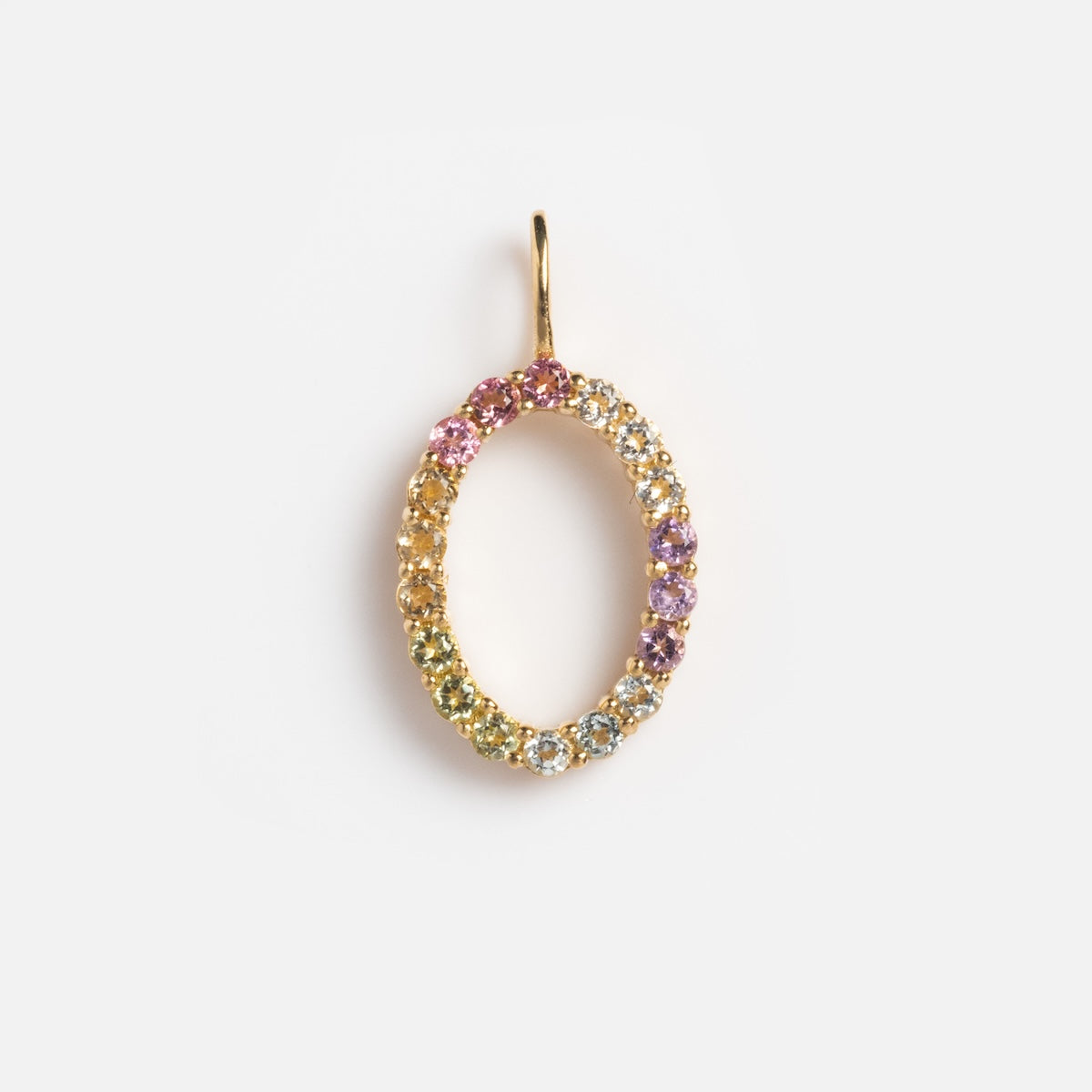 The Solid Gold Pastel Gemstone Letter Charm Sample is a 9k yellow gold oval pendant encrusted with small multicolored gemstones, including pink tourmaline, in a gradient pattern and shown on a plain white background.