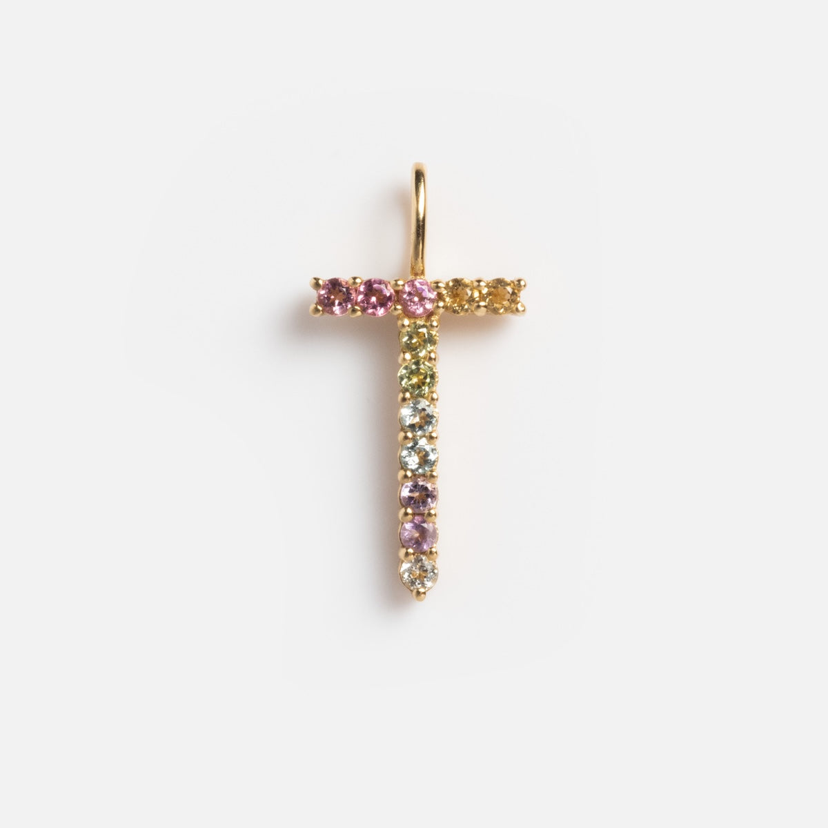 The Solid Gold Pastel Gemstone Letter Charm Sample features the letter T, crafted in 9k yellow gold and decorated with colorful gemstones—including pink tourmaline—in vertical and horizontal rows on a plain white background.