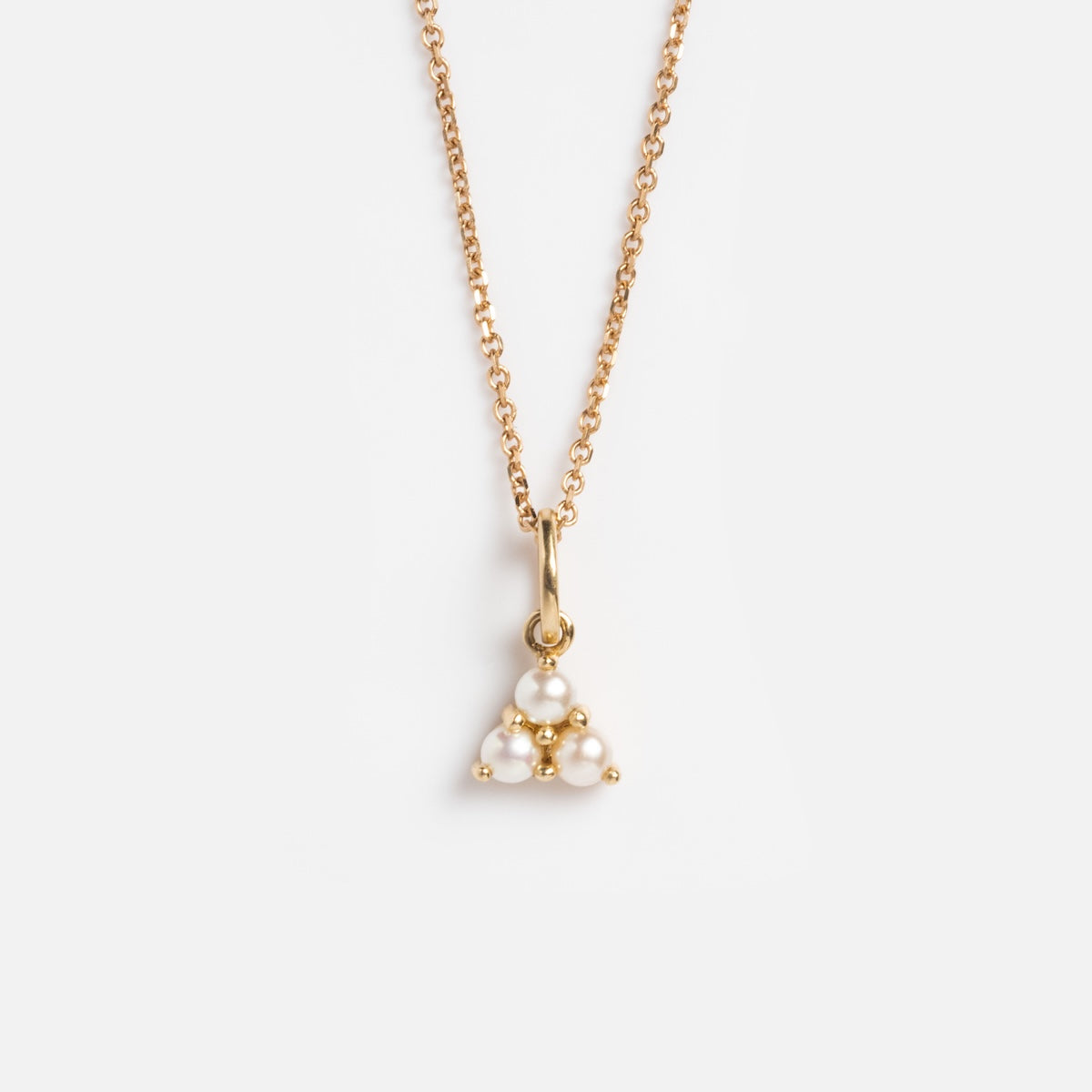 The Solid Gold Luminous Pearl Trio Necklace features a delicate gold chain with a triangular pendant of clustered white pearls, displayed on a plain white background.