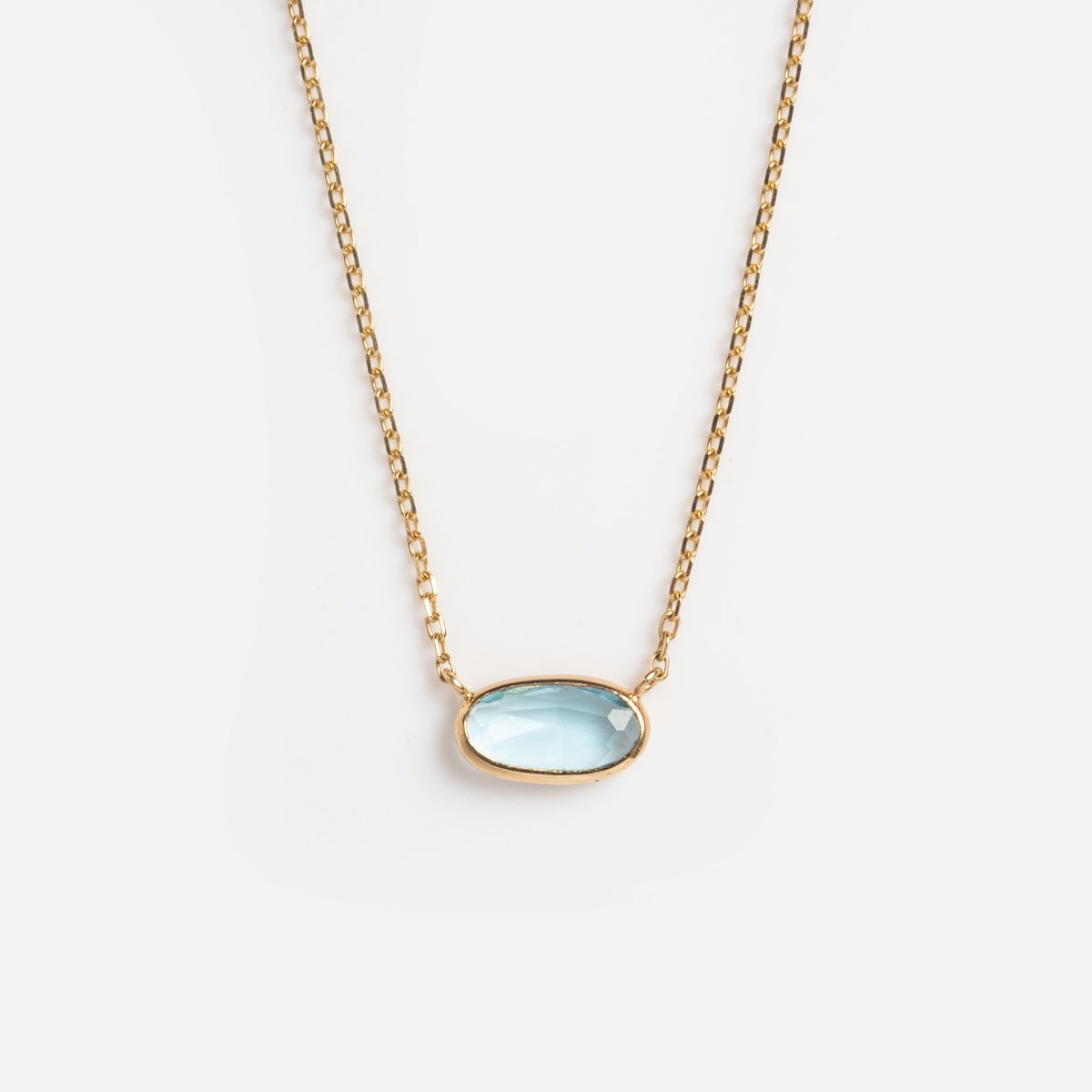 The Solid Gold Daybreak Swiss Blue Topaz Necklace features an oval-shaped Swiss blue topaz pendant in a simple gold bezel, shown on a plain white background. It belongs to the timeless Family Gold collection.