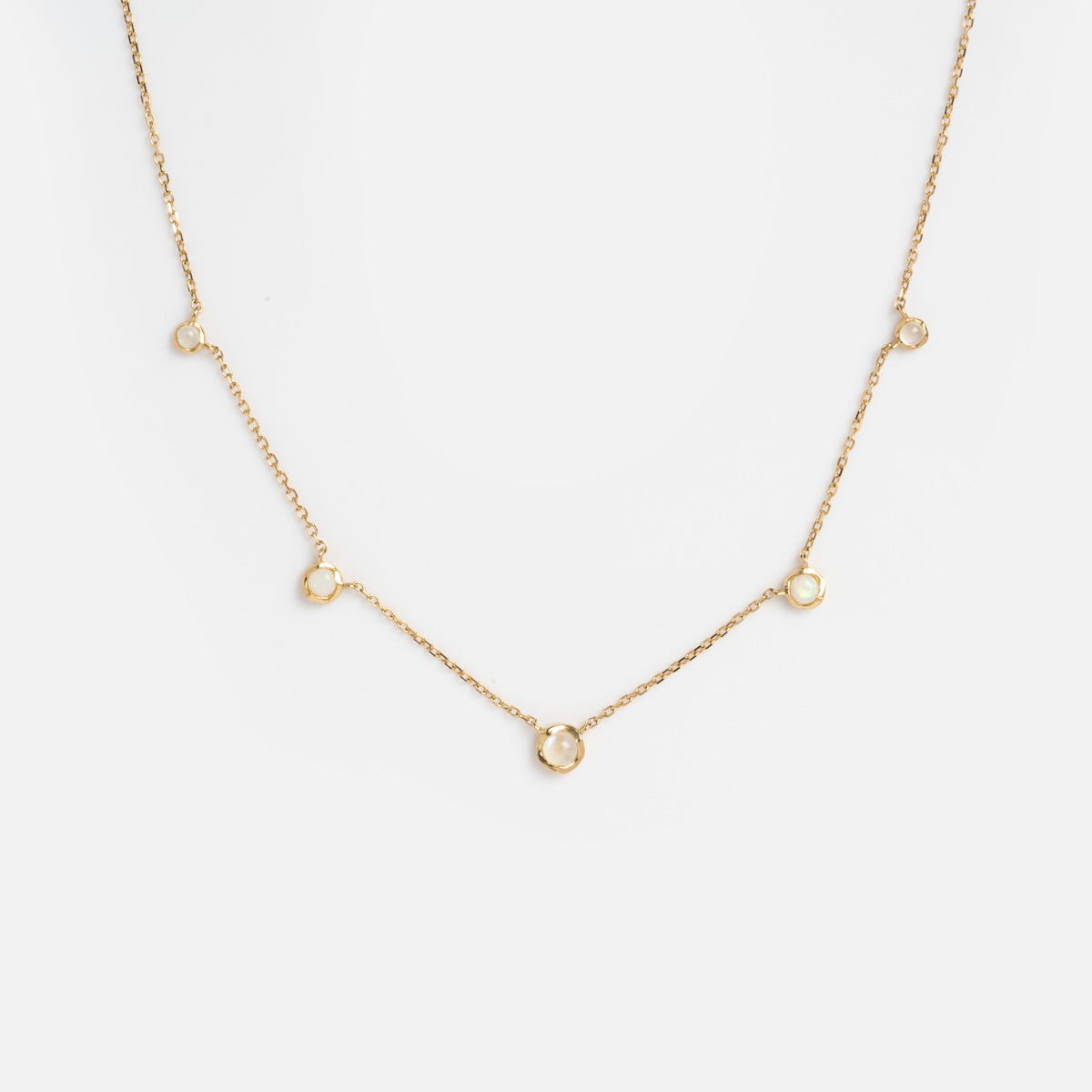 The Solid Gold Horizon Moonstone and Opal Sprinkle Necklace features five small, evenly spaced circular pendants, displayed against a plain white background.