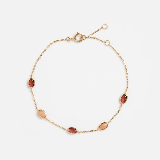 The Solid Gold Sunlit Garnet and Sunstone Bracelet features five bezel-set oval gemstones—three garnets and two sunstones—with a spring ring clasp and adjustable end. Shown on a white background.